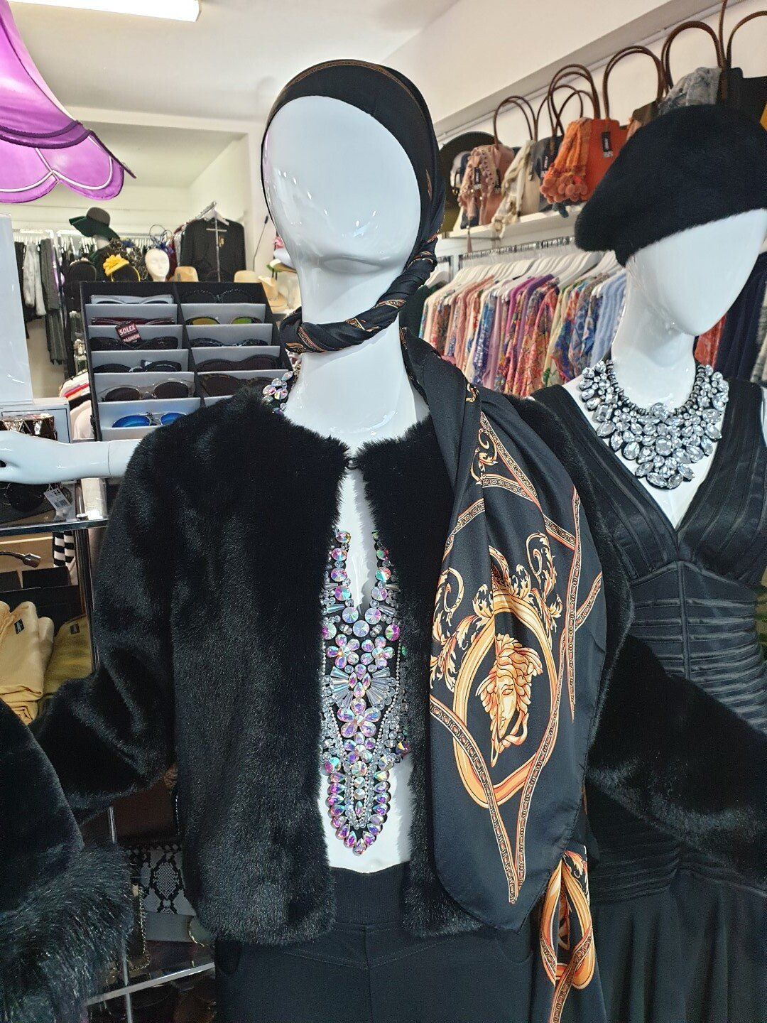 Mannequins in a store wearing black faux fur jacket, scarf, and a Versace handbag.