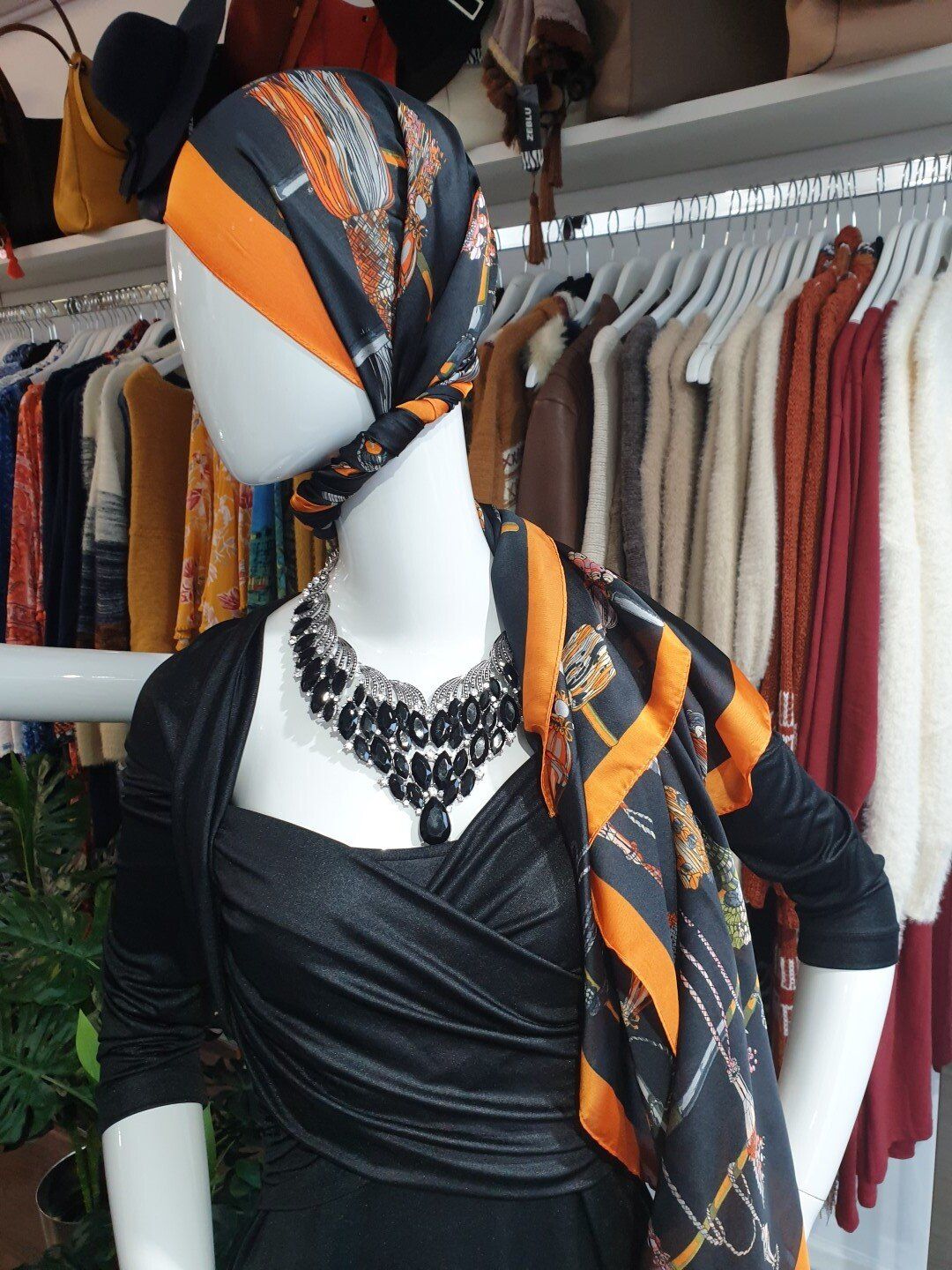 Mannequin in a black dress, scarf, and necklace. The scarf is black and orange; setting appears to be a clothing store.