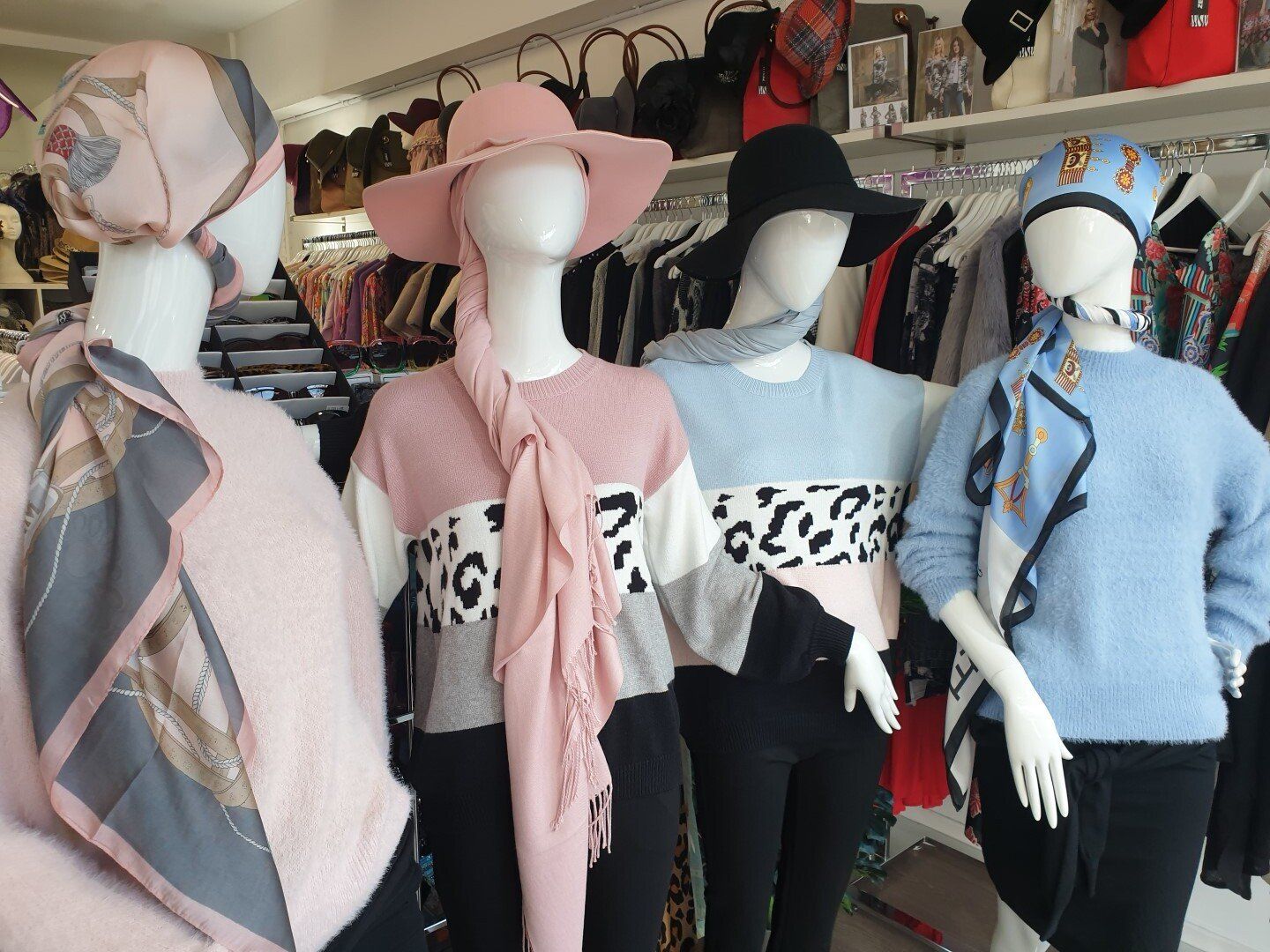 Four mannequins in a clothing store wearing sweaters, hats, and scarves.  Shop setting.