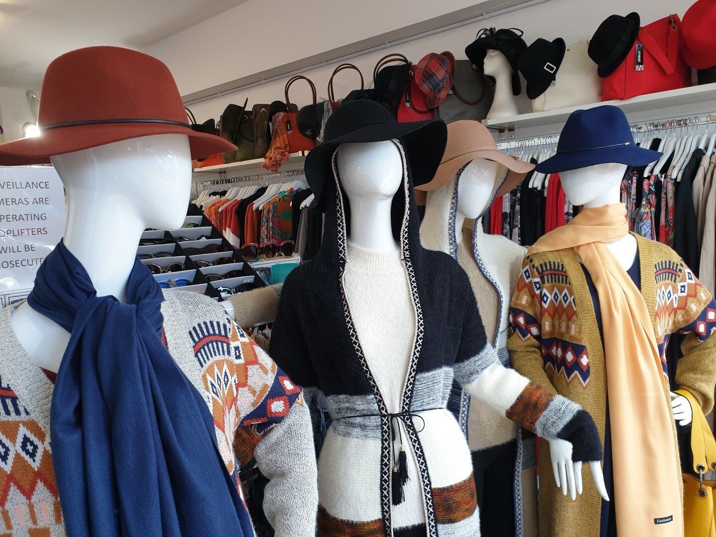 Mannequins wearing hats and sweaters in a clothing store.