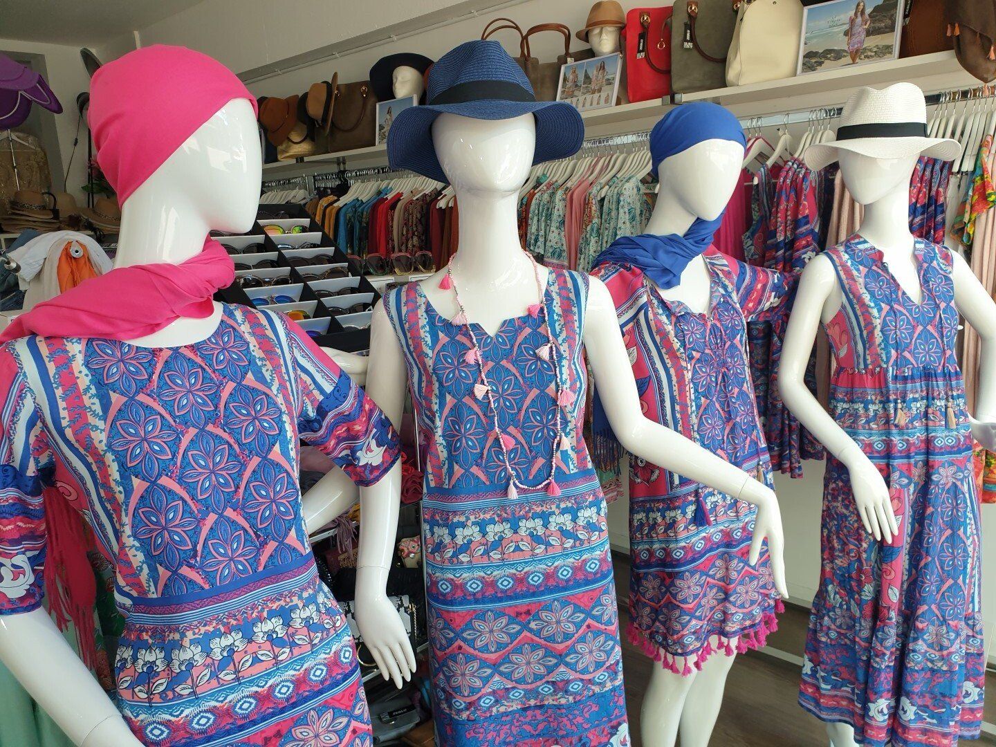 Four mannequins wearing blue and pink patterned dresses, in a clothing store.