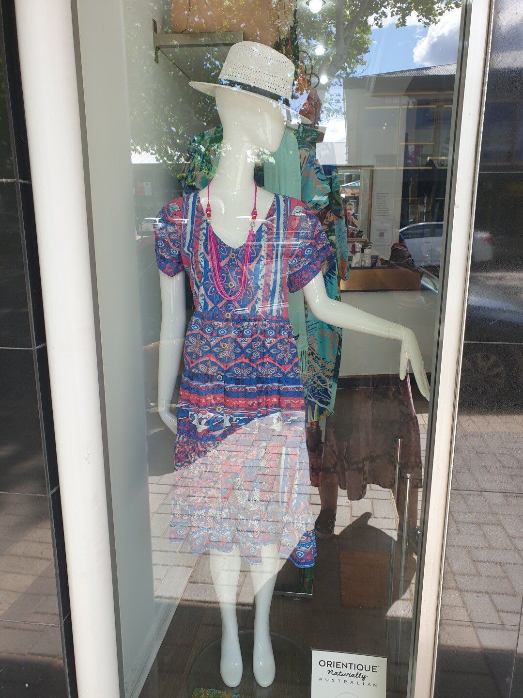 Mannequin in a store window wearing a patterned dress, hat, and necklace.