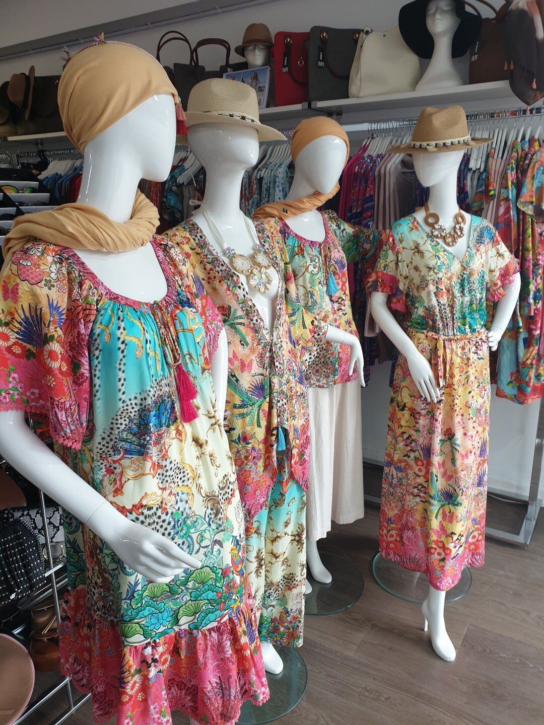 Four mannequins in a shop, wearing colorful floral dresses and accessories.
