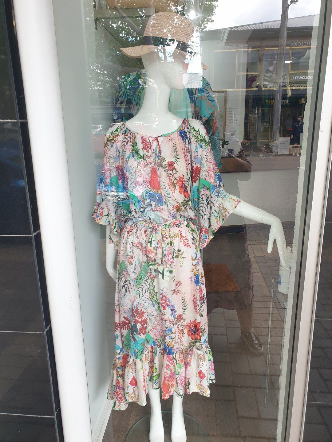 Mannequin in floral dress and straw hat in a shop window.