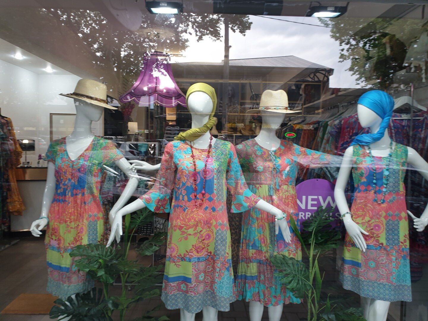 Four mannequins in colorful dresses, hats, and headscarves displayed in a storefront window.