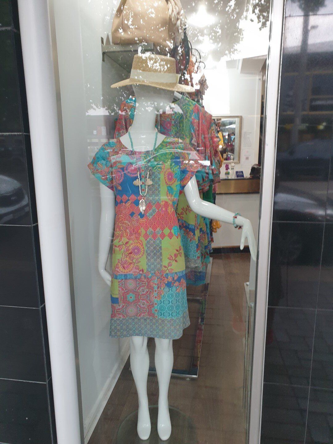 Mannequin in a colorful patchwork dress, wearing a hat, displayed in a shop window.