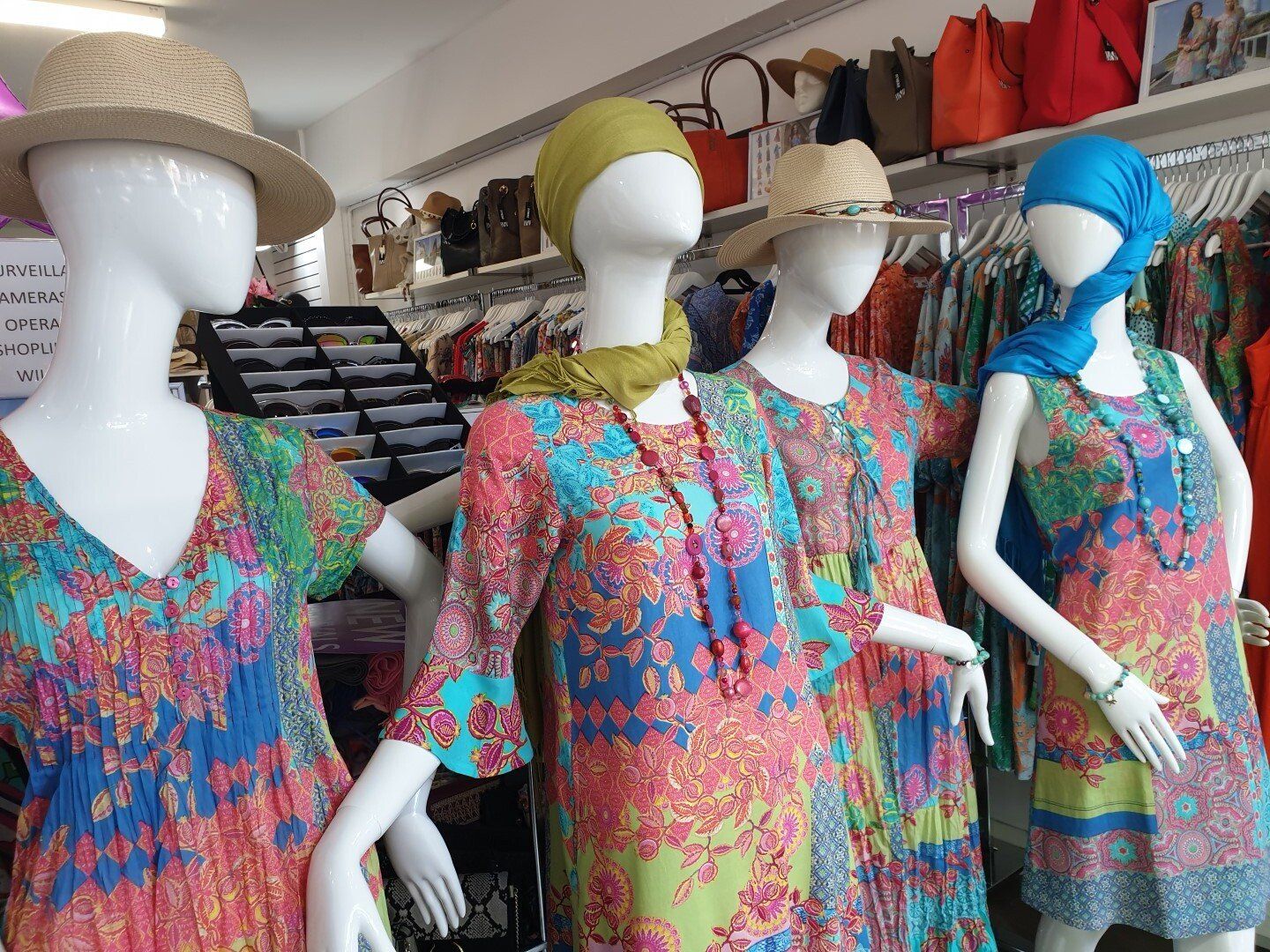 Four mannequins in a clothing store; vibrant patterned dresses, hats, and scarves displayed.