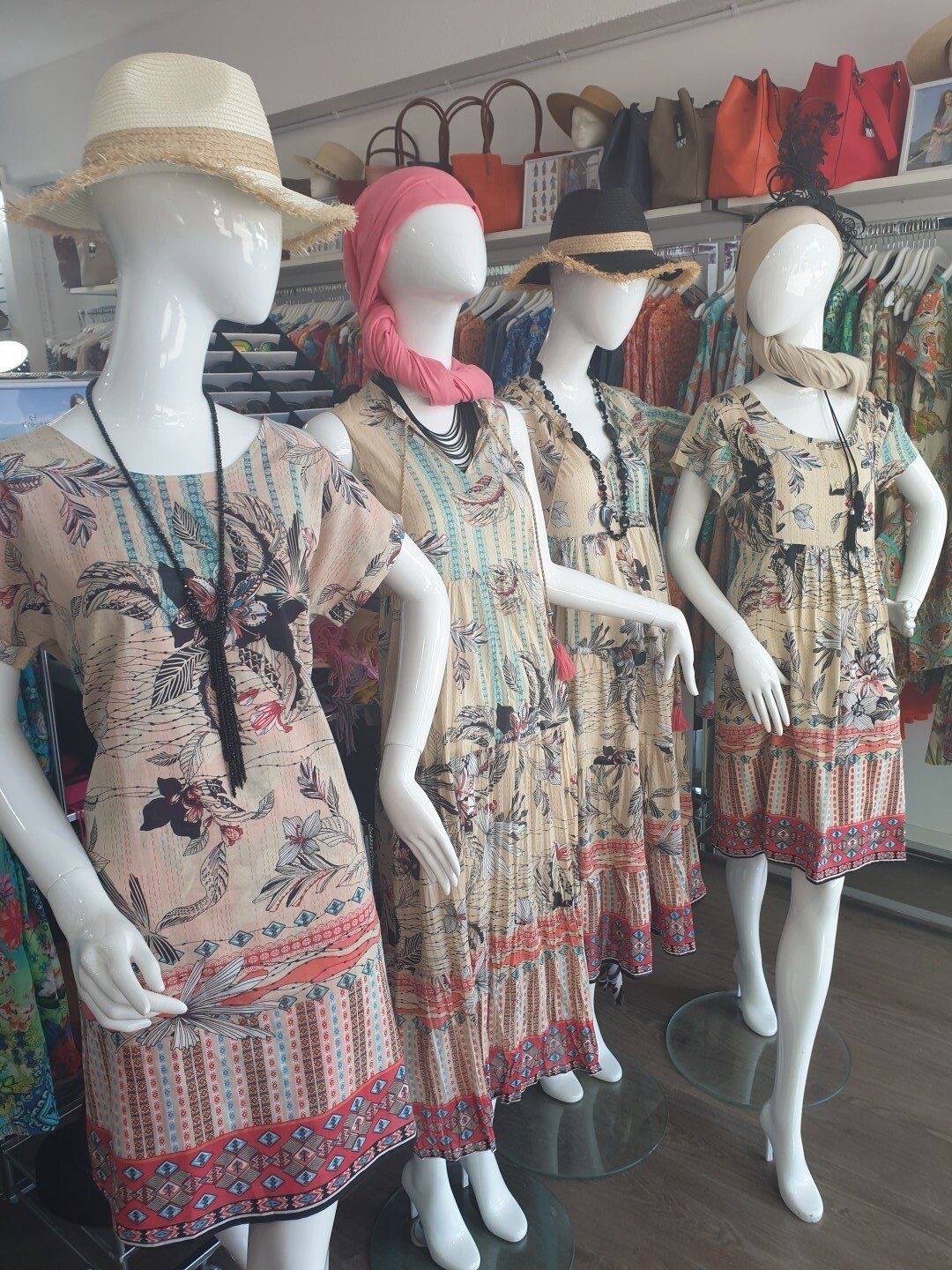 Four mannequins in a clothing store, each wearing a patterned dress, hat, and scarf.