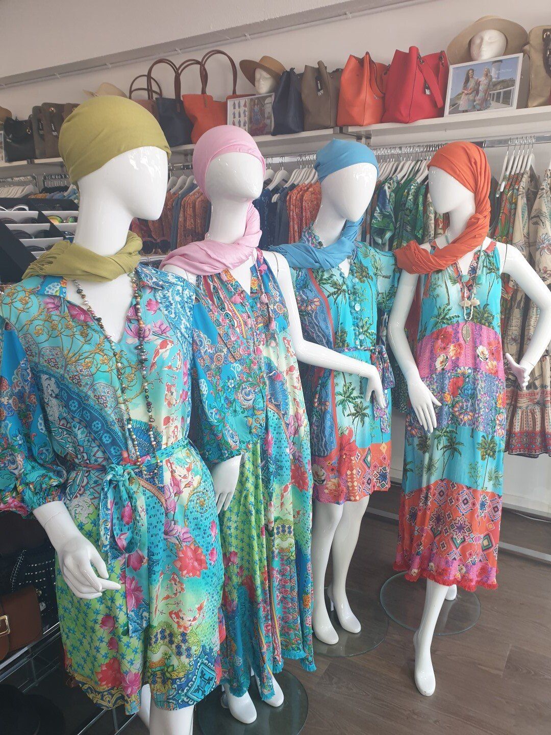 Four mannequins in a shop window wearing colorful floral dresses and headscarves.