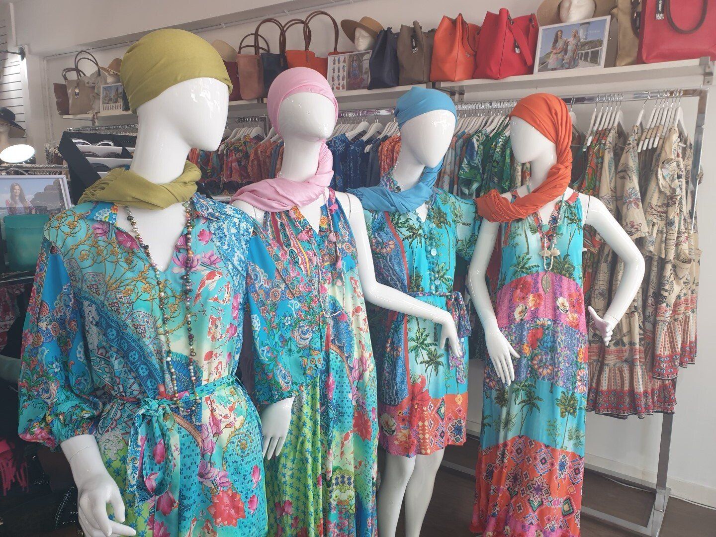 Four mannequins in colorful patterned dresses and headscarves in a shop.