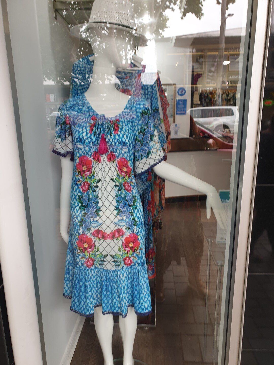 Mannequin in blue floral dress in a shop window.