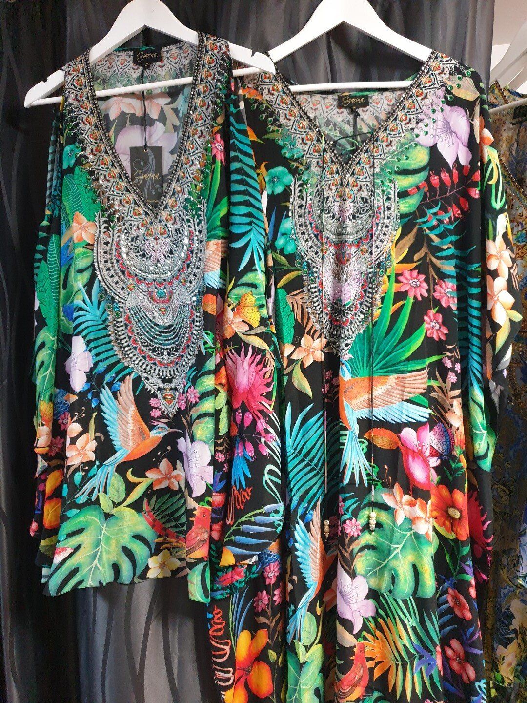 Two floral patterned, open-shoulder tops hanging on white hangers.