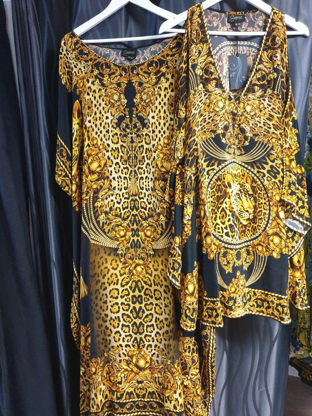 Two gold and black patterned tops hanging on white hangers against a dark background.