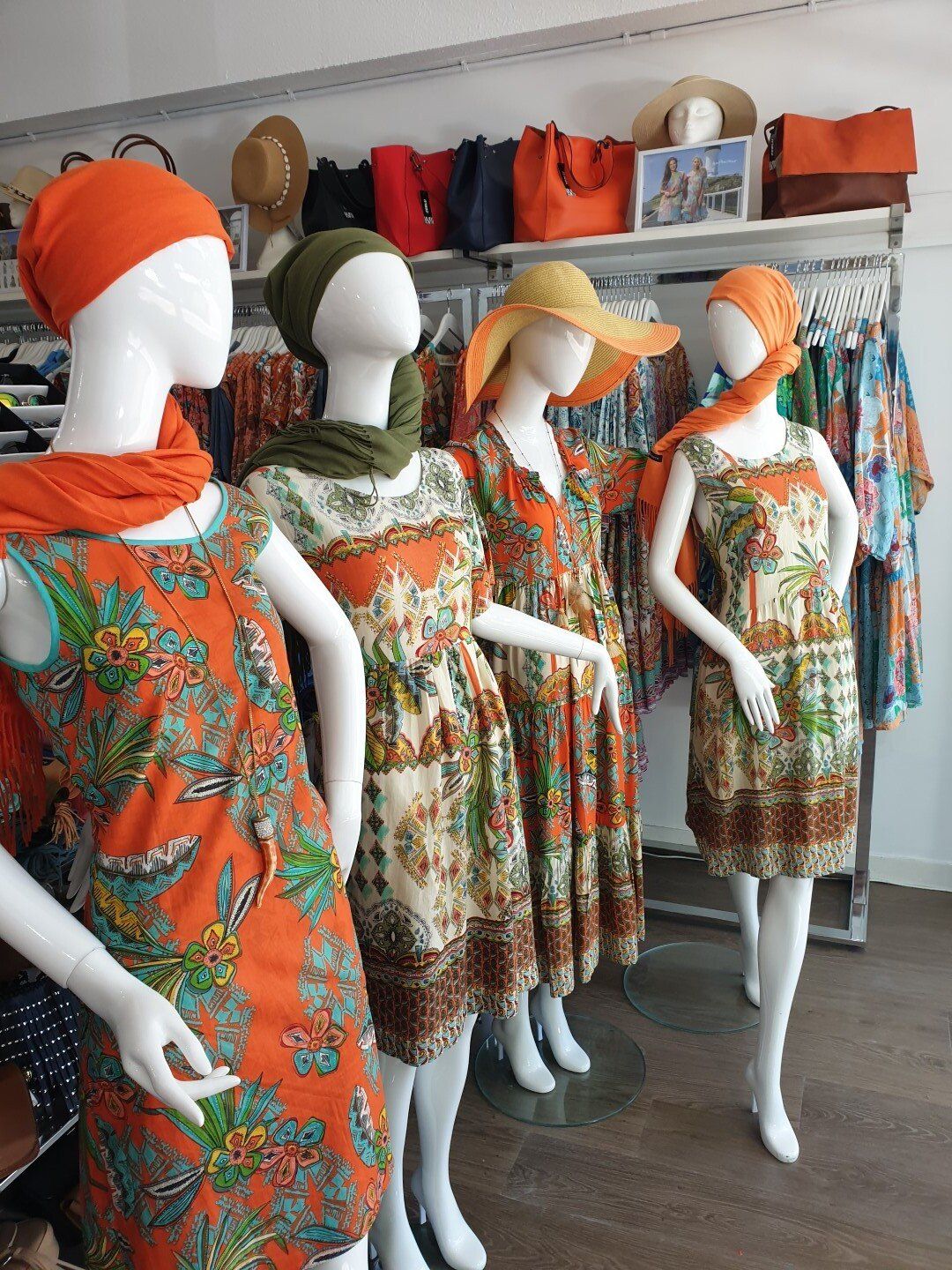 Four mannequins in a shop display dresses and headwear, in an array of orange and floral prints.