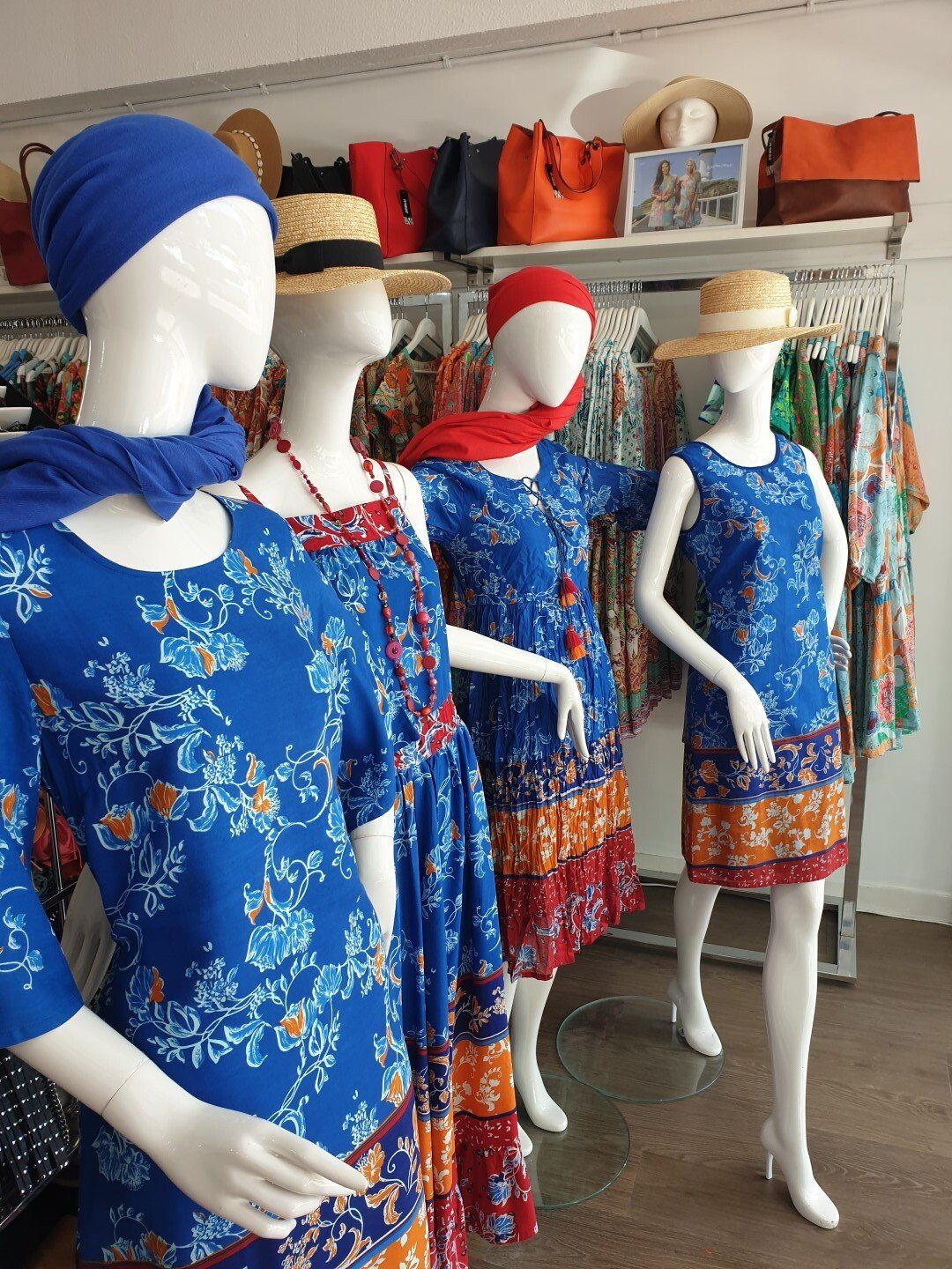 Four mannequins in a store wearing blue floral dresses, scarves, and hats; shelves with accessories in the background.