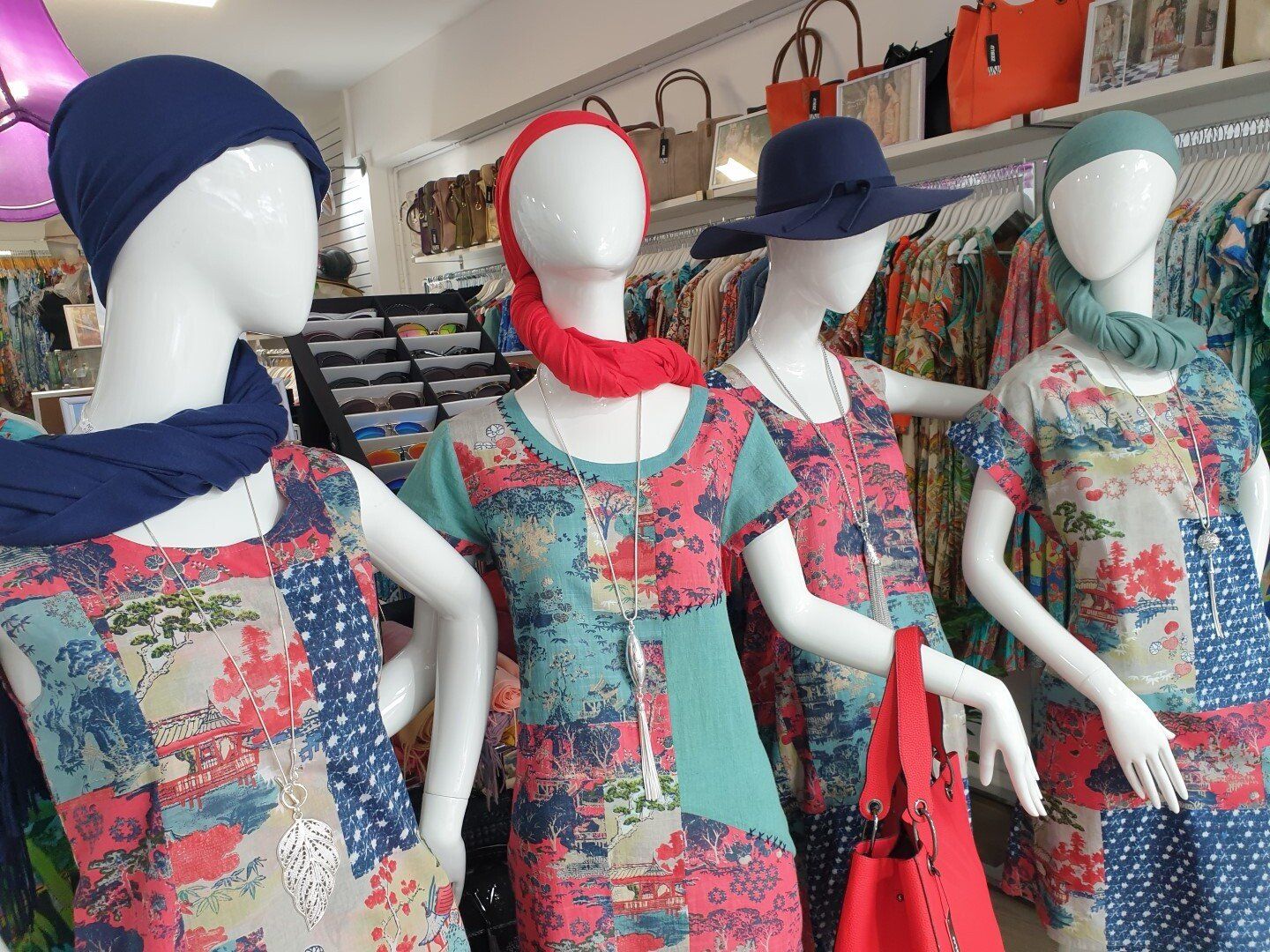 Four mannequins in a clothing store, wearing colorful patterned dresses and scarves.