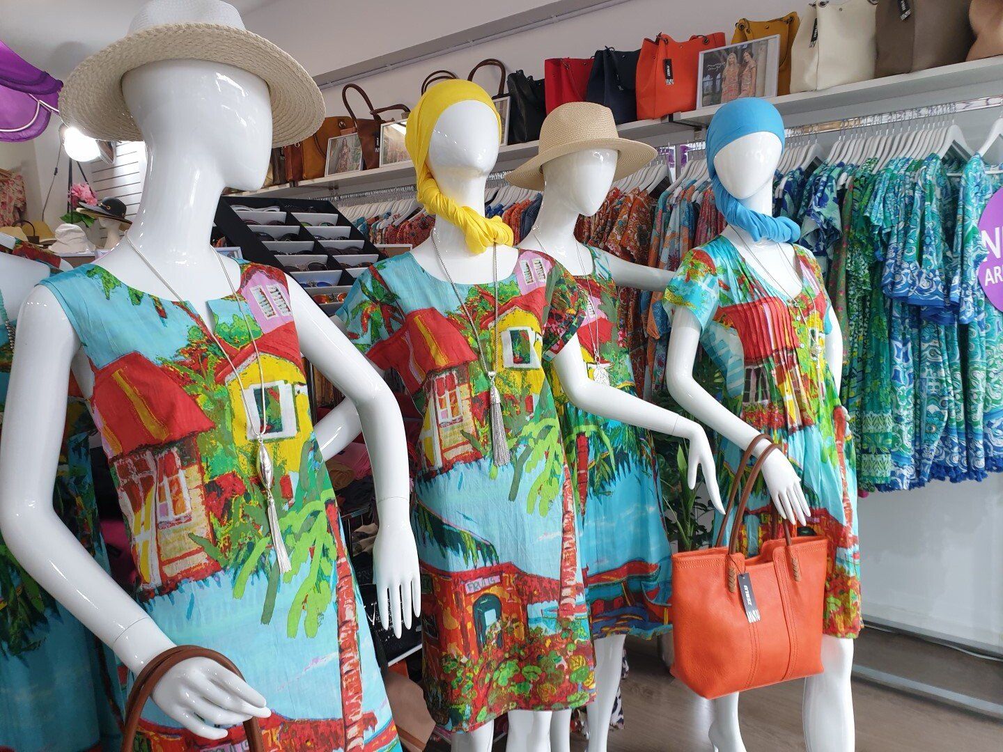 Four mannequins in a clothing store wearing turquoise print dresses with bags.
