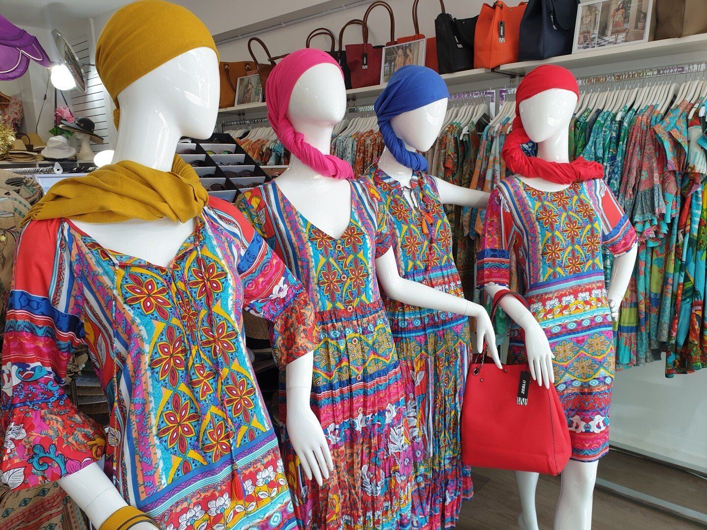 Four mannequins in a clothing store wearing colorful patterned dresses and headscarves.