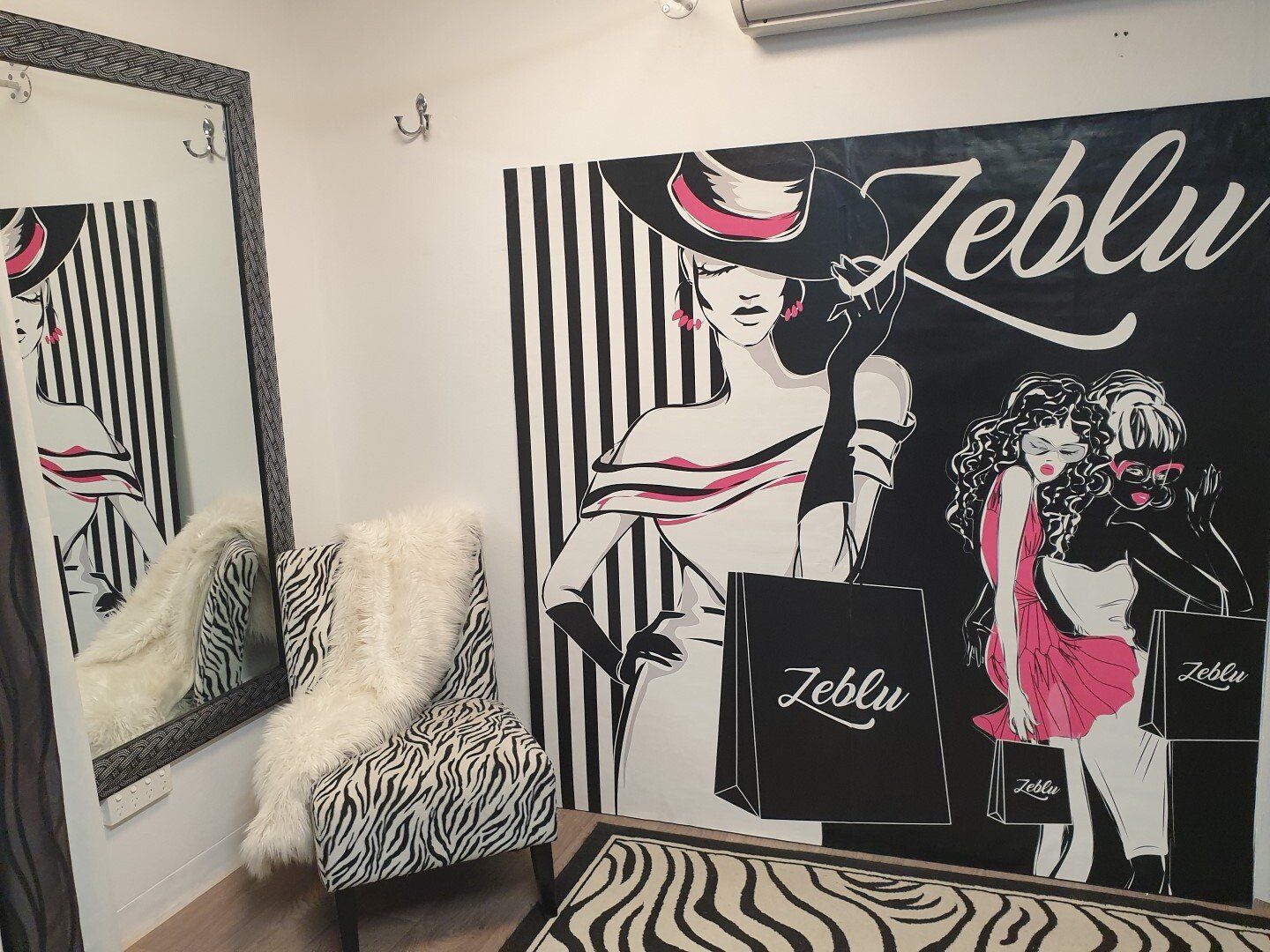 Zebra-print chair with fur, wall mural with fashion illustration, and mirror. Black and white striped wall.
