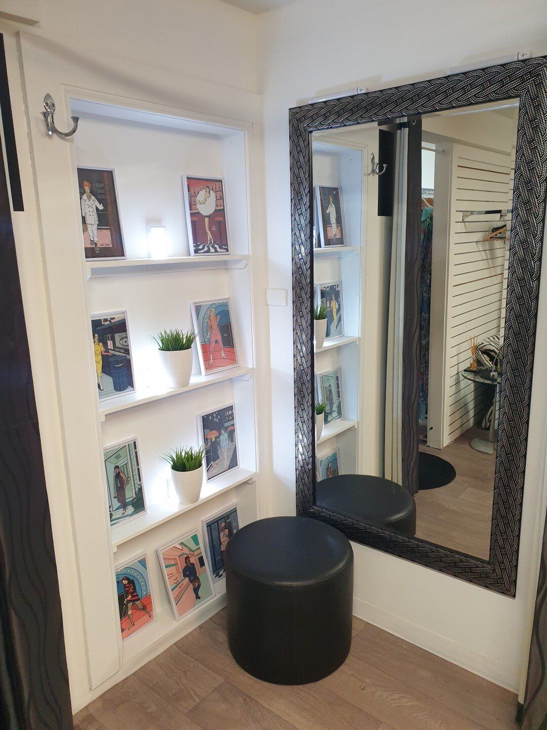 Corner of a retail space with shelves displaying magazines, a decorative mirror, and a black stool.