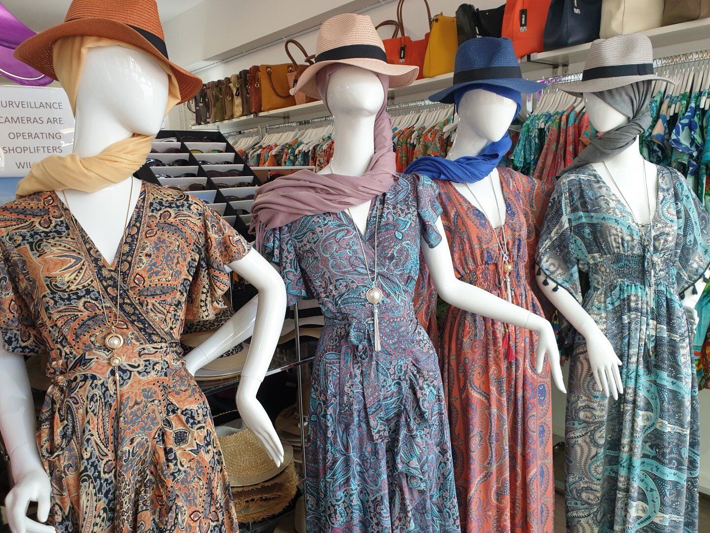 Four mannequins in a store display colorful summer dresses, each wearing a hat and scarf.