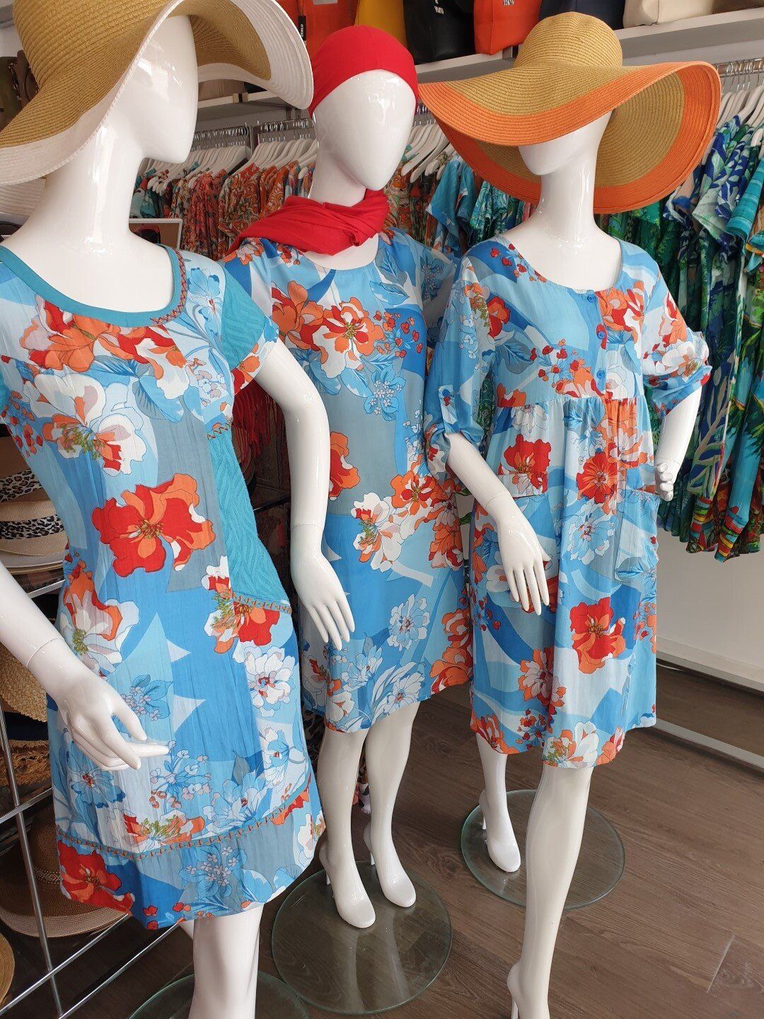 Three mannequins wearing blue floral dresses and sun hats.