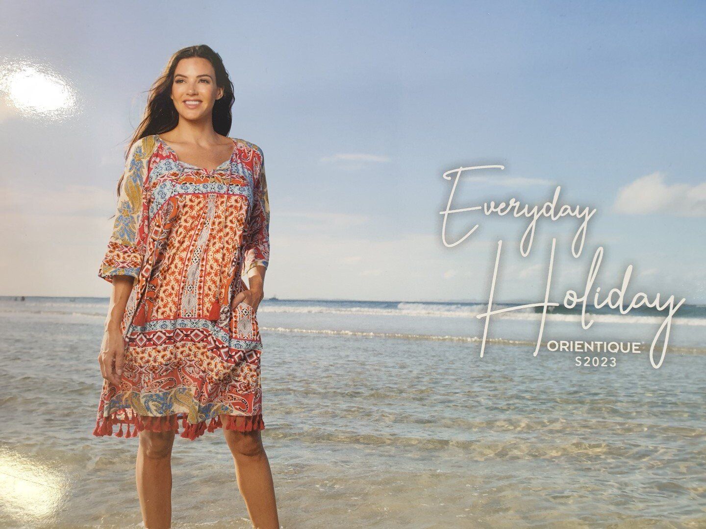 Woman in patterned dress smiles on a beach. 