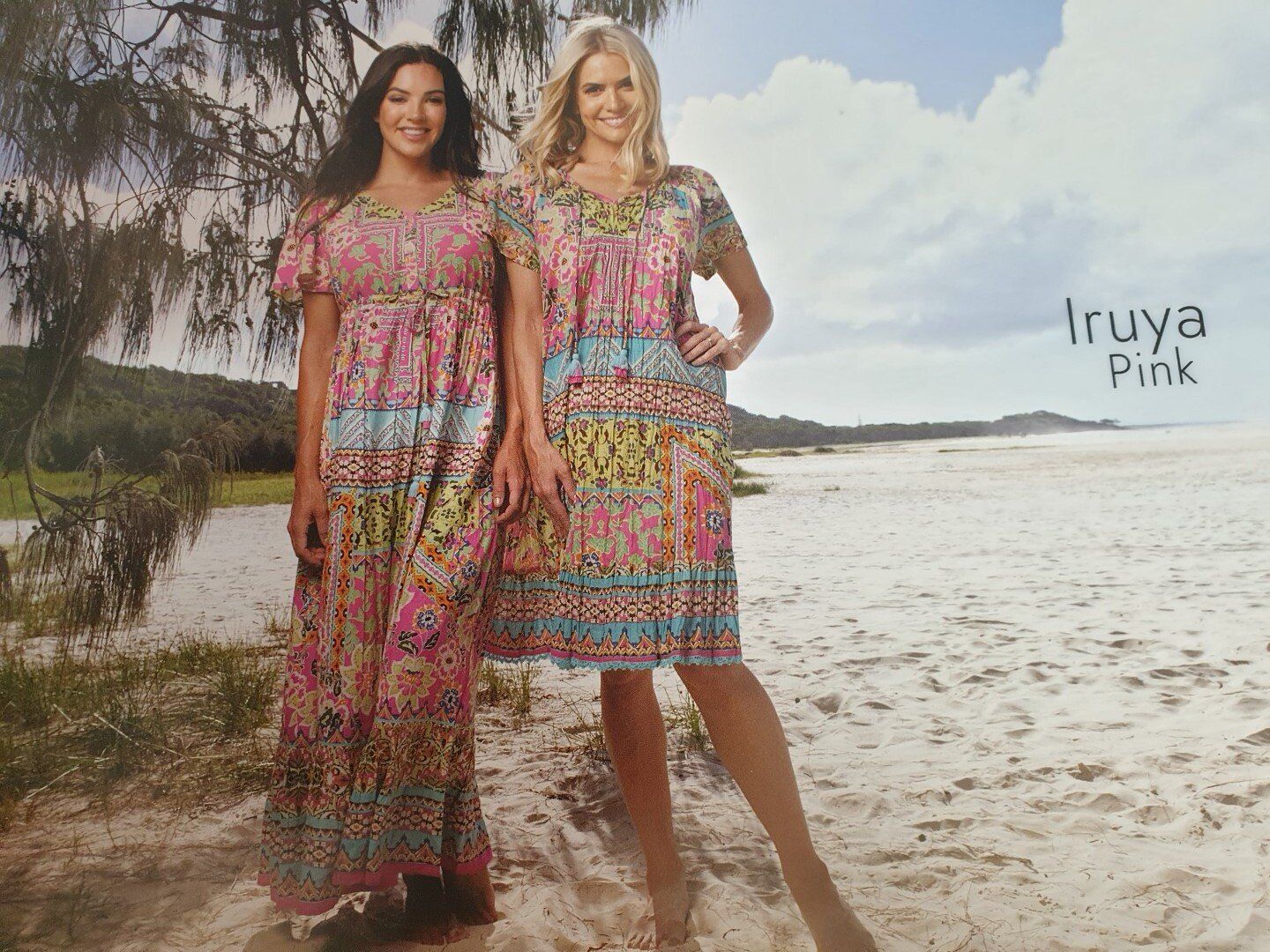 Two women in pink patterned dresses on a beach. One is full-length, the other is knee-length.