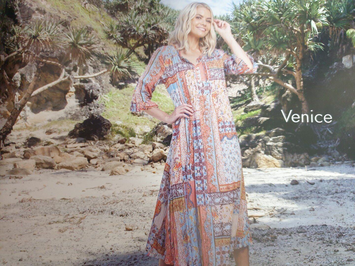 Woman in patterned maxi dress, standing on a beach. Venice written on the right.