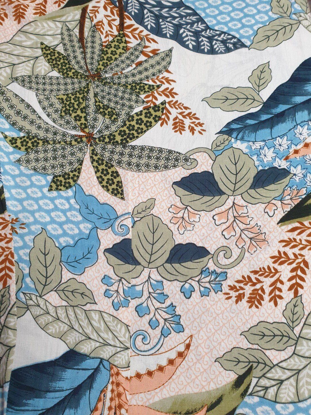 Floral fabric with a mix of leaves, in shades of blue, green, brown, and peach on a light background.