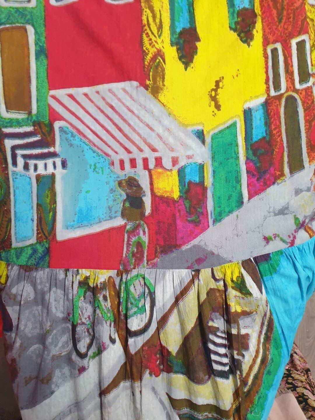 Colorful street scene: figure with bicycle, shops, red, yellow, blue buildings.