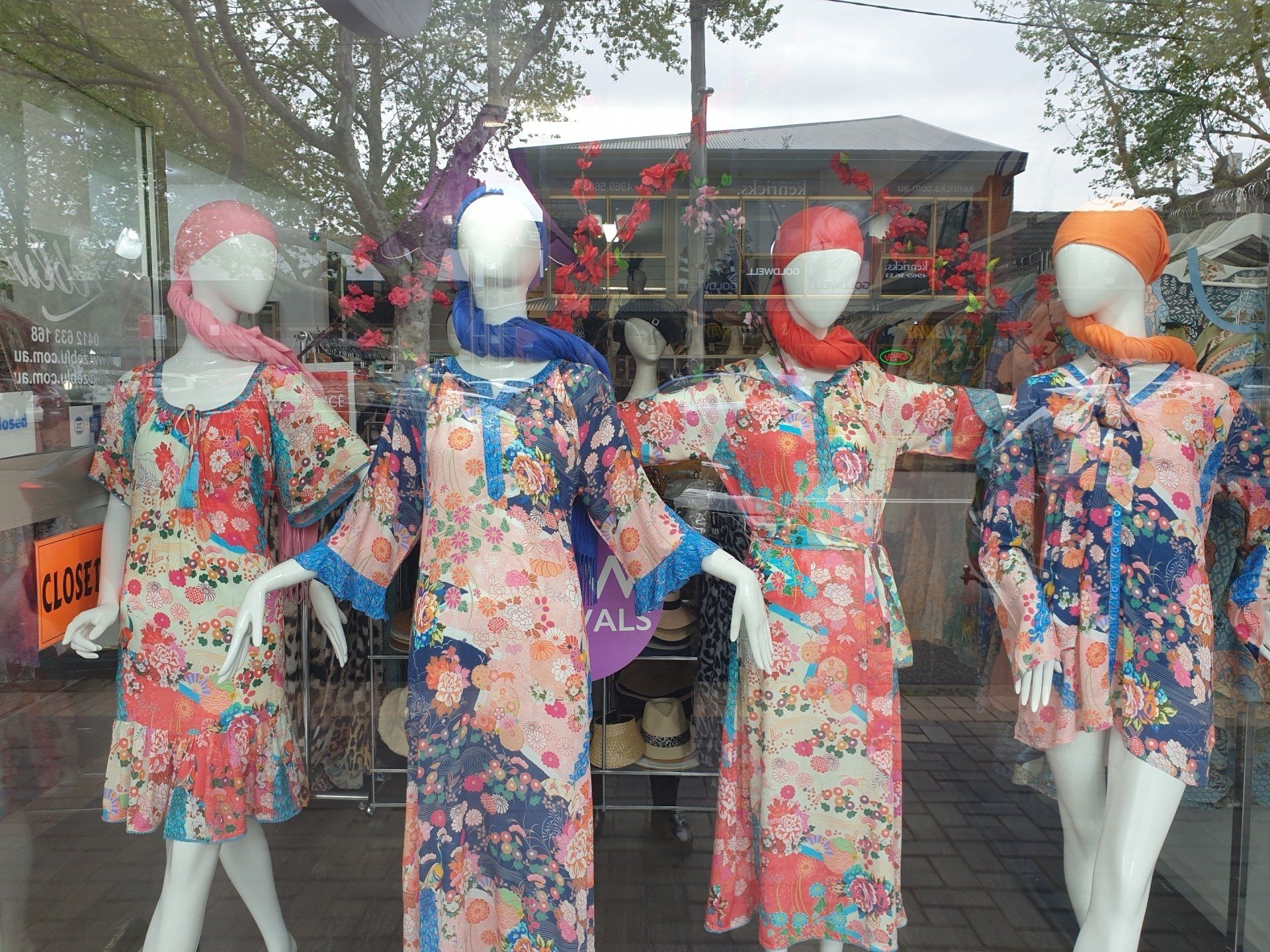 Four mannequins wearing floral print dresses and scarves in a shop window display.