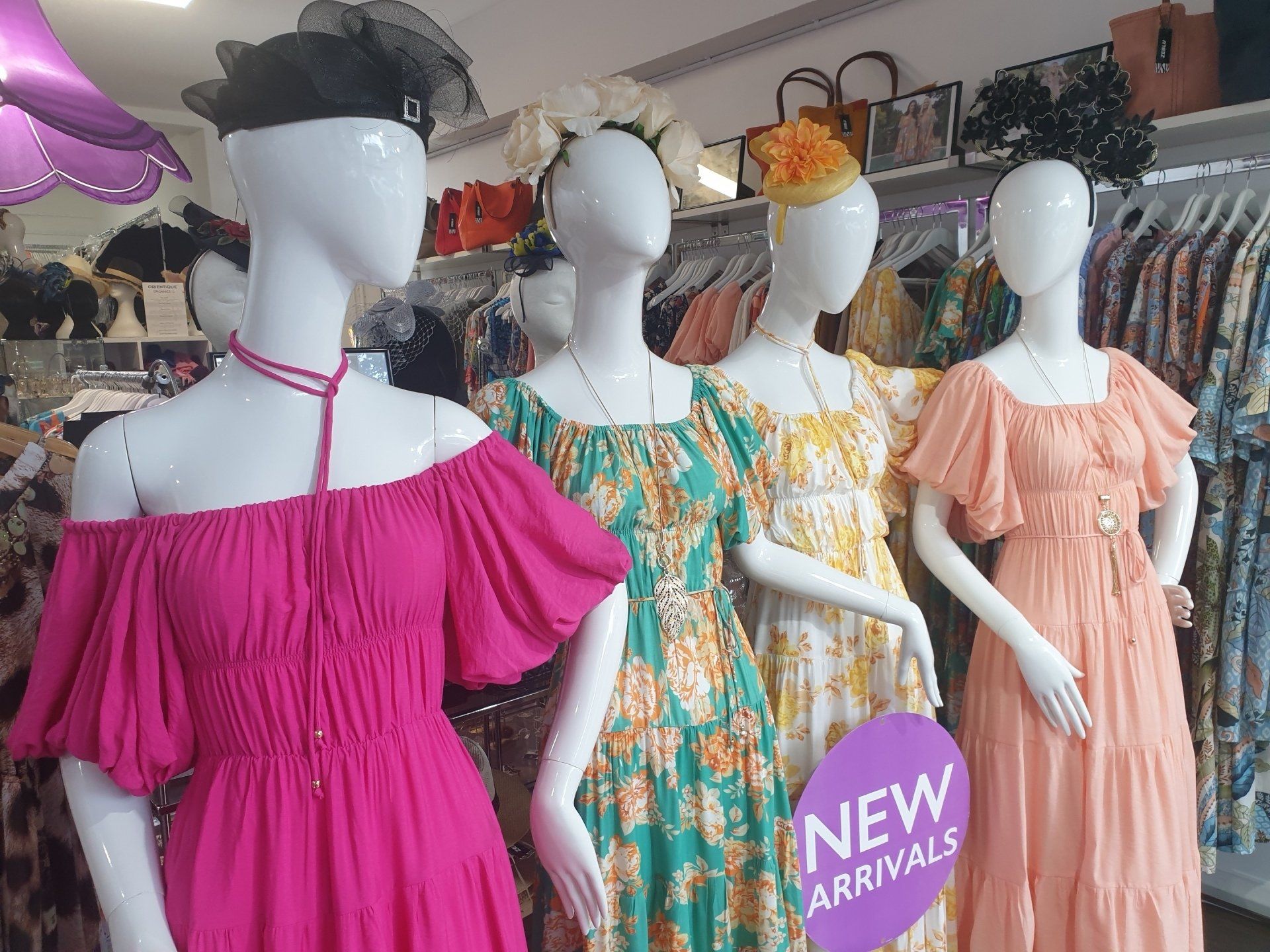 Mannequins in a clothing store display dresses in pink, green, yellow, and peach colors. 