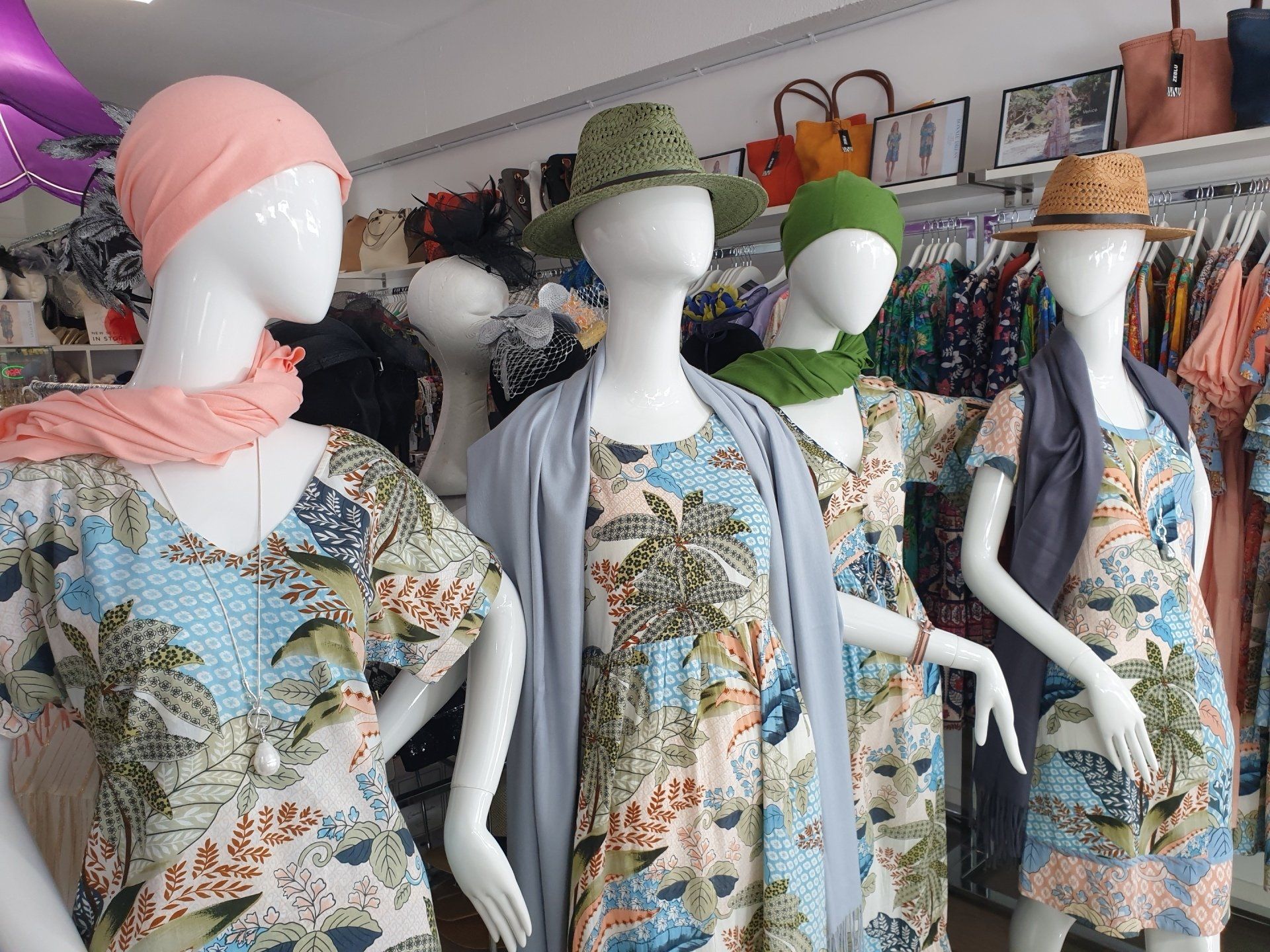 Four mannequins in a clothing store display floral dresses, hats, and scarves.