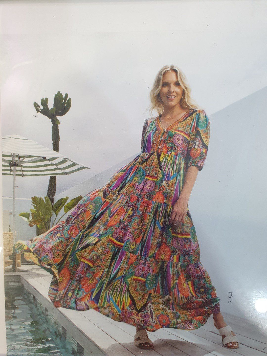 Woman in floral maxi dress stands by a pool, posing.