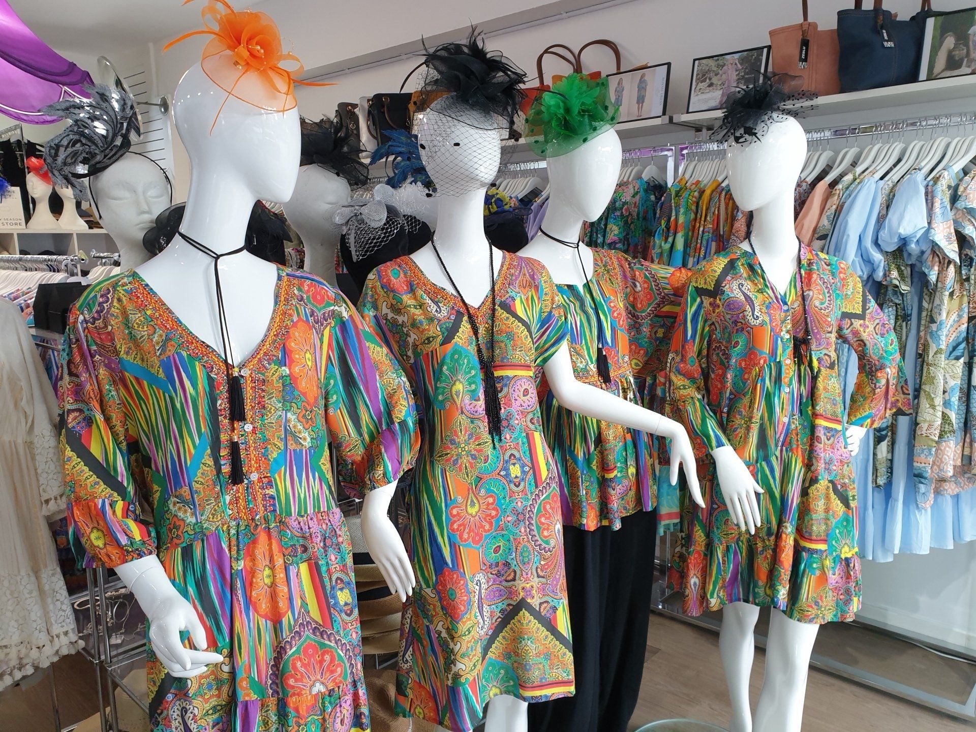 Four mannequins wearing patterned dresses and hats in a clothing store.