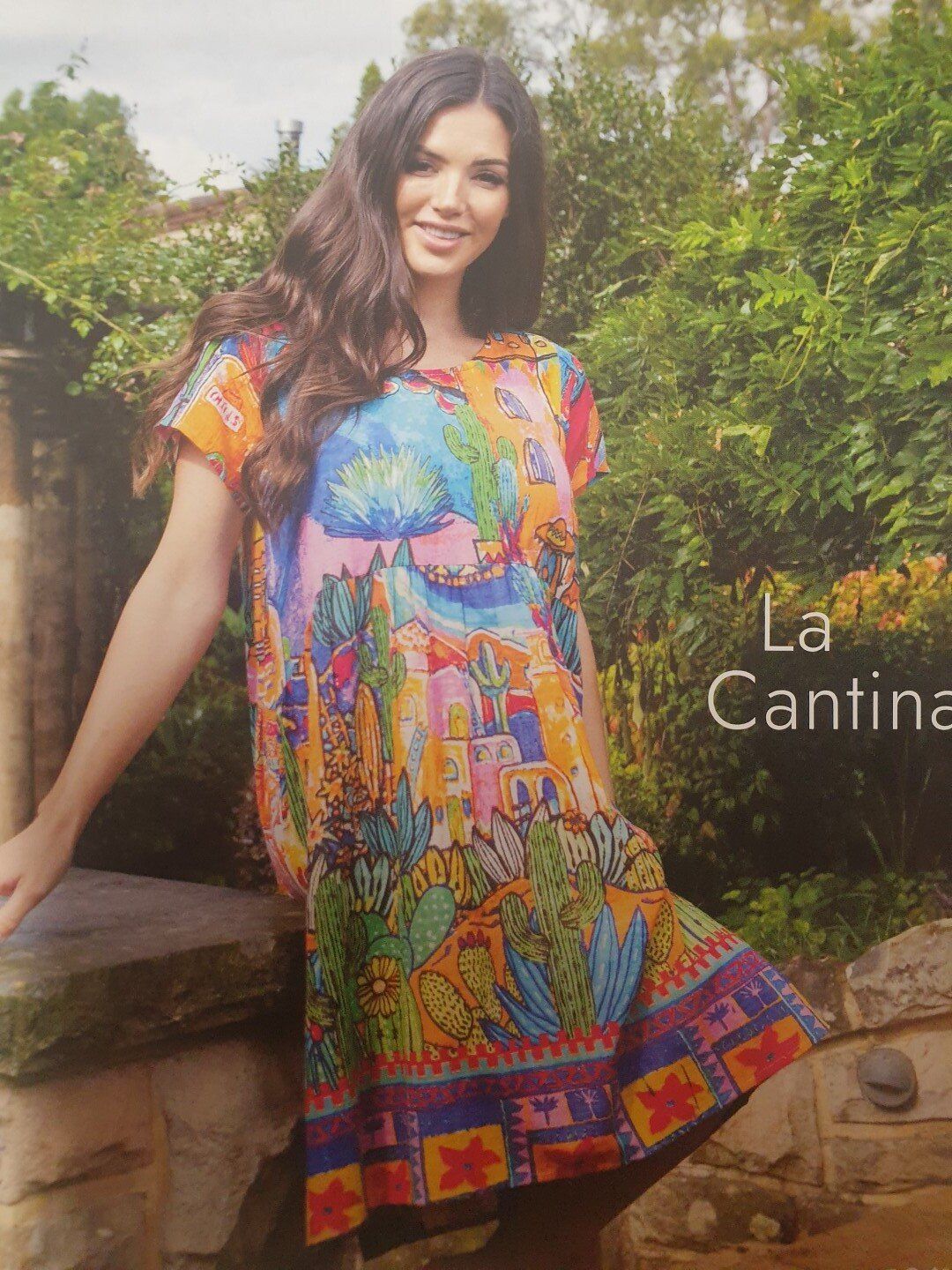 Woman in a colorful printed dress smiles outdoors.