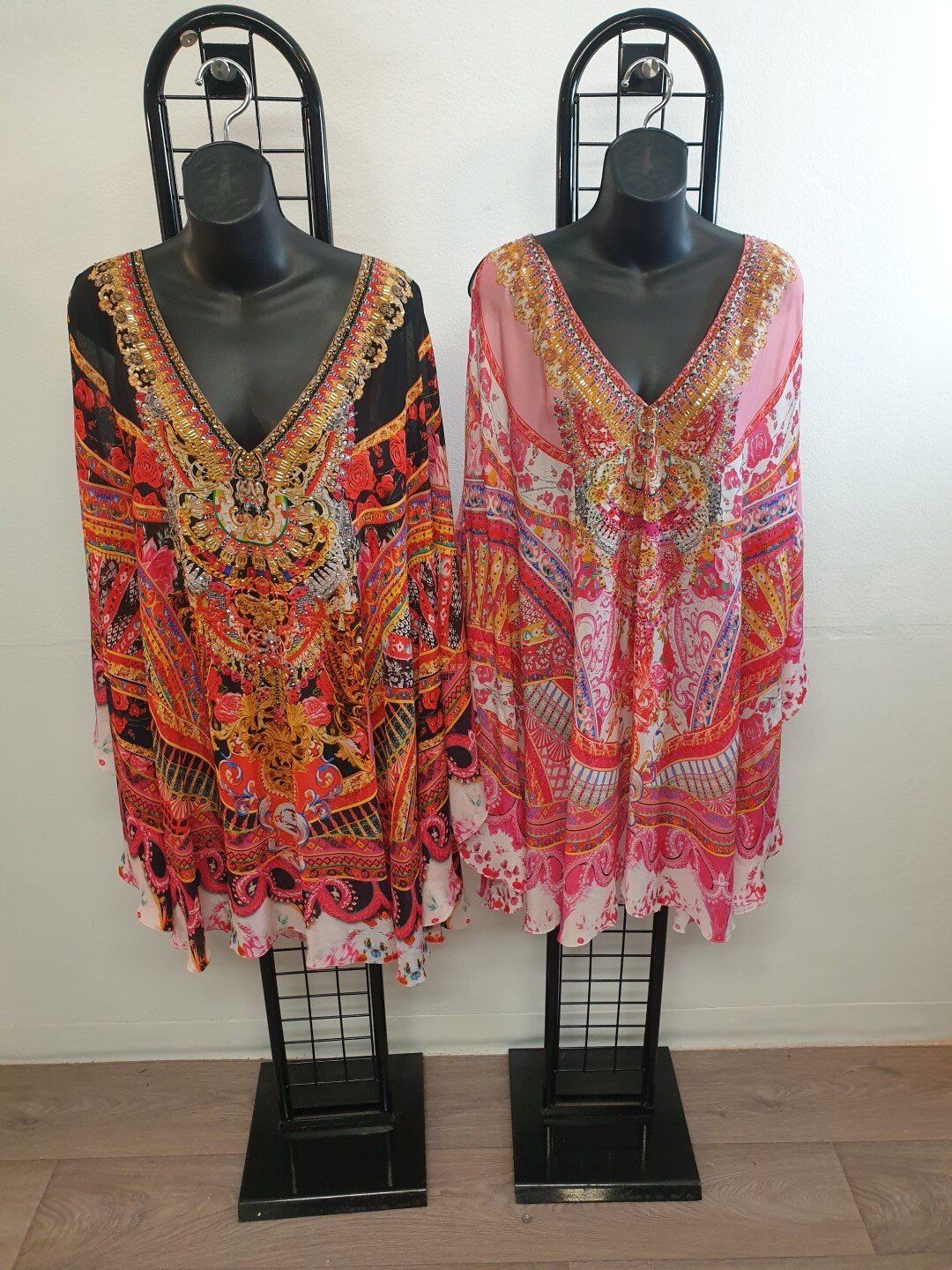 Two patterned tunics on black mannequins. One is orange/black, the other is pink.