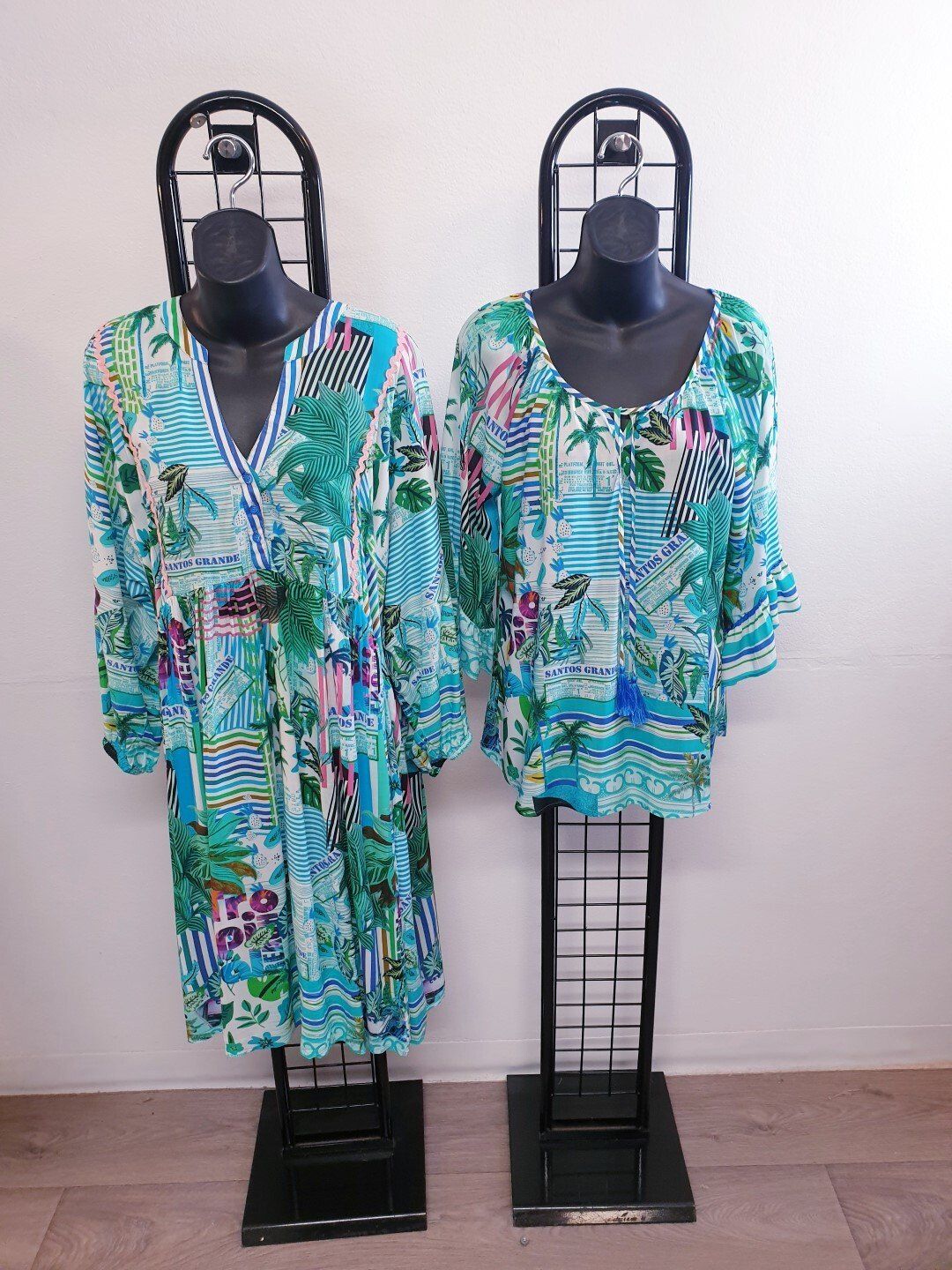 Two mannequins display turquoise, floral-patterned tops on black stands against a white wall.