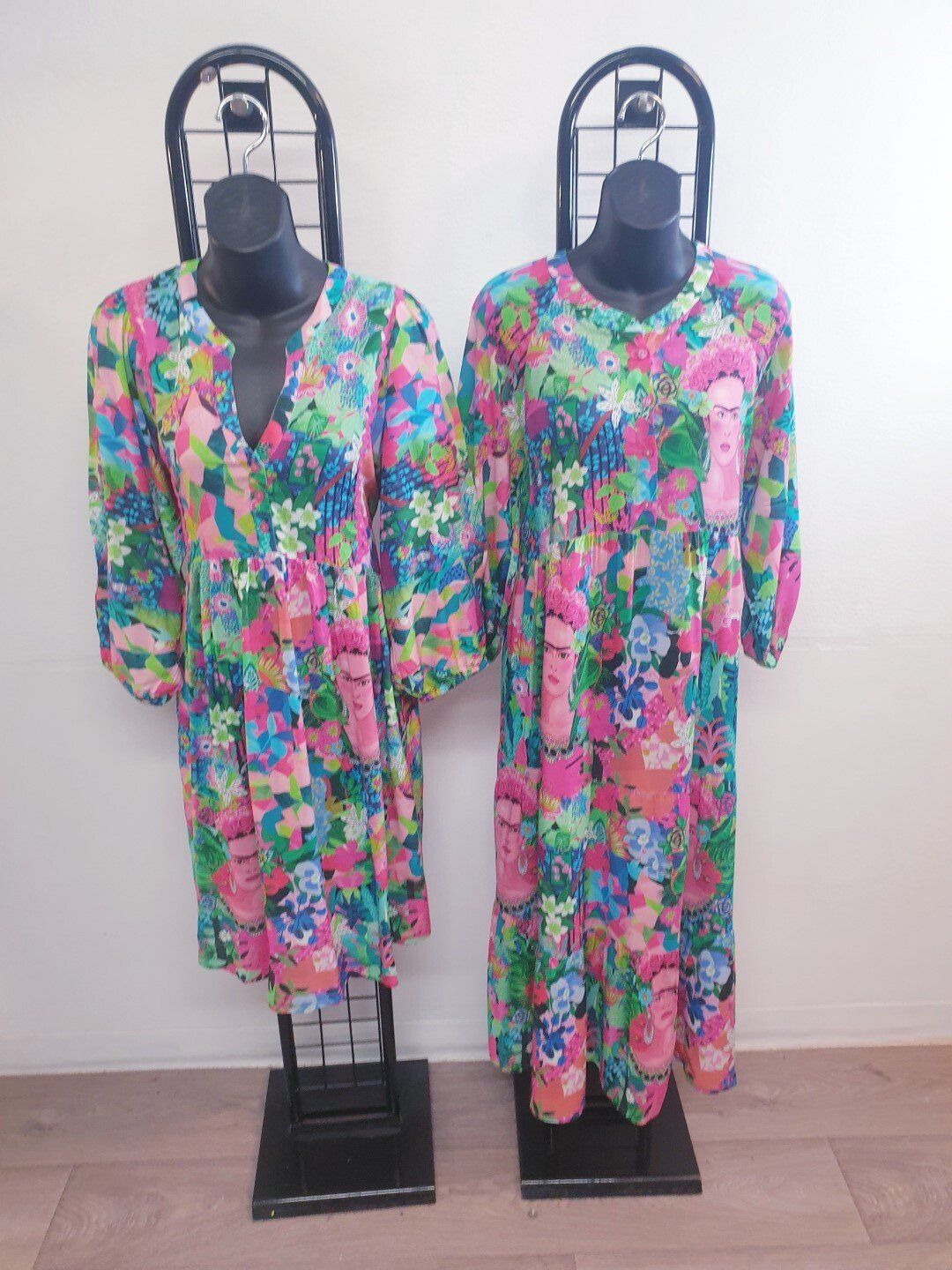 Two floral print dresses on black mannequins.