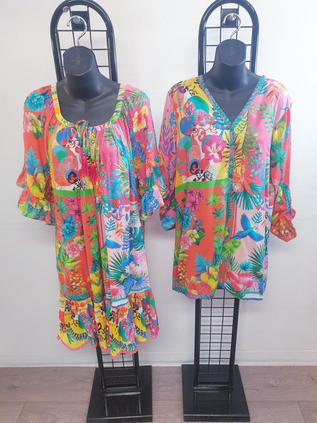 Two colorful floral print dresses on black mannequins.
