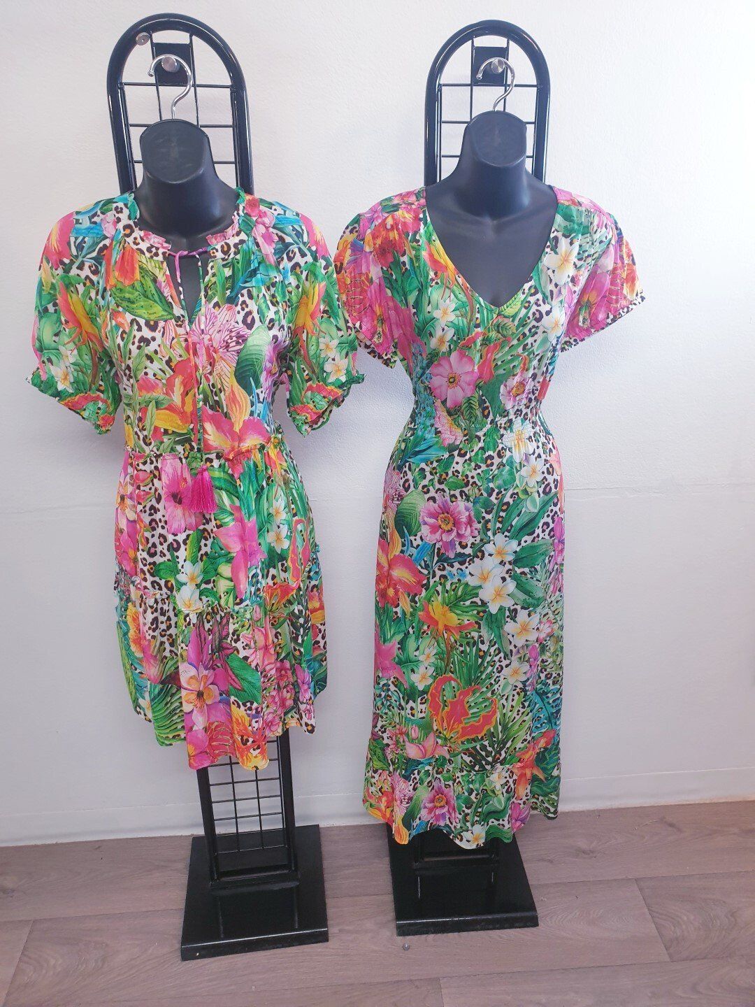 Two mannequins wearing brightly colored floral print dresses.