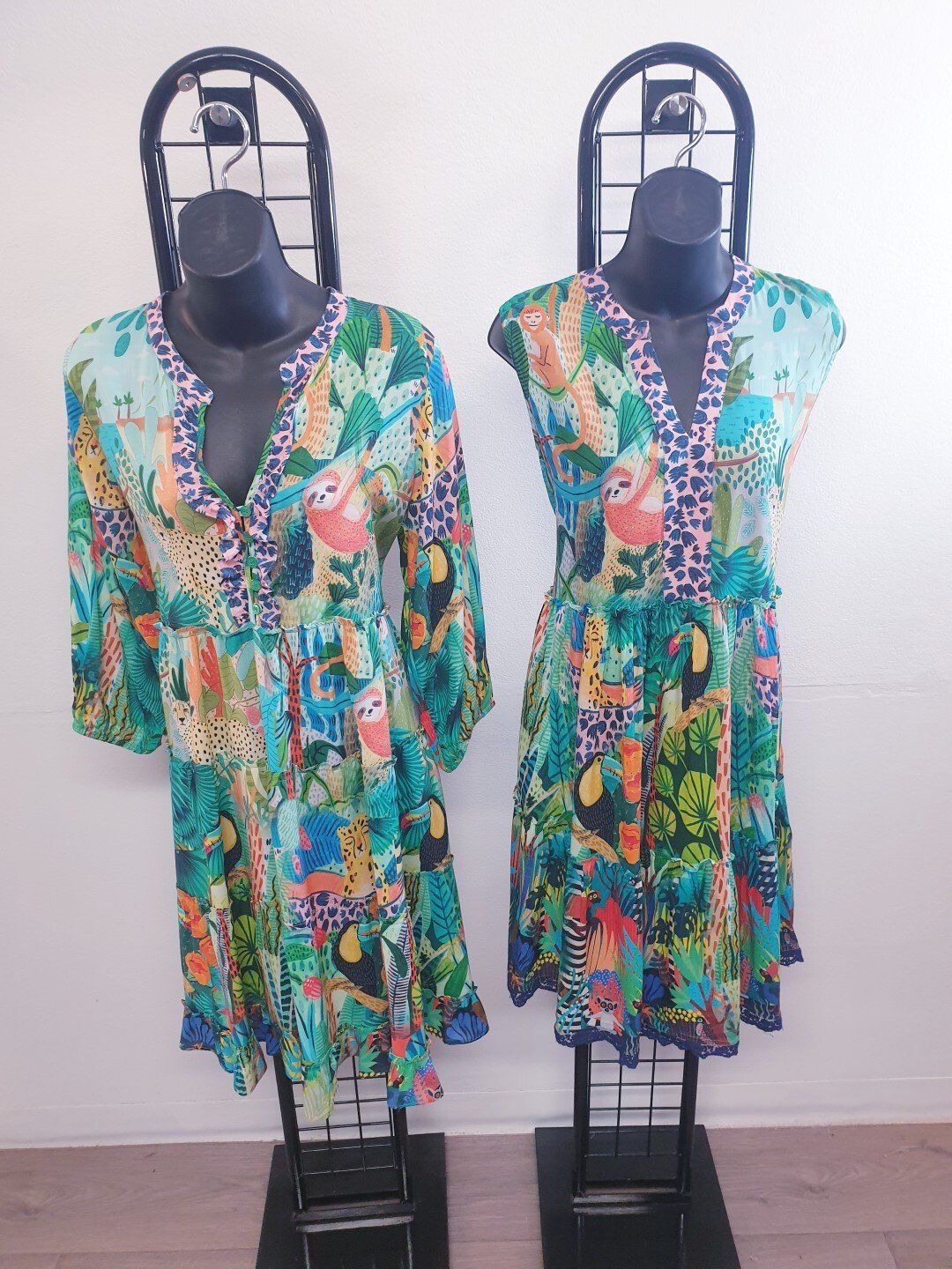 Two colorful patterned dresses on display mannequins. Blue, green, and pink tropical print with a V-neck.