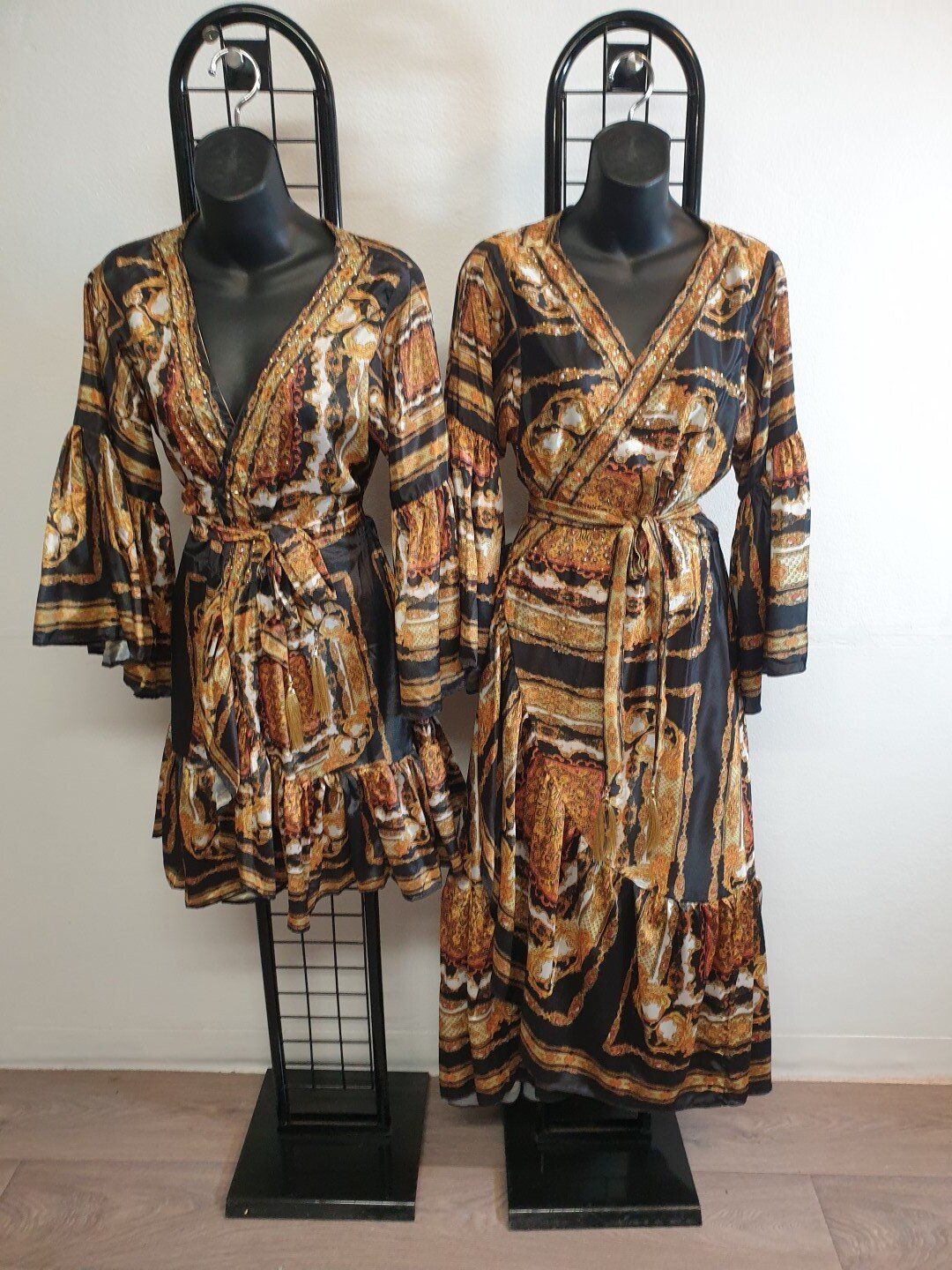Two mannequins wearing patterned wrap dresses, one short, one long, on black display racks.