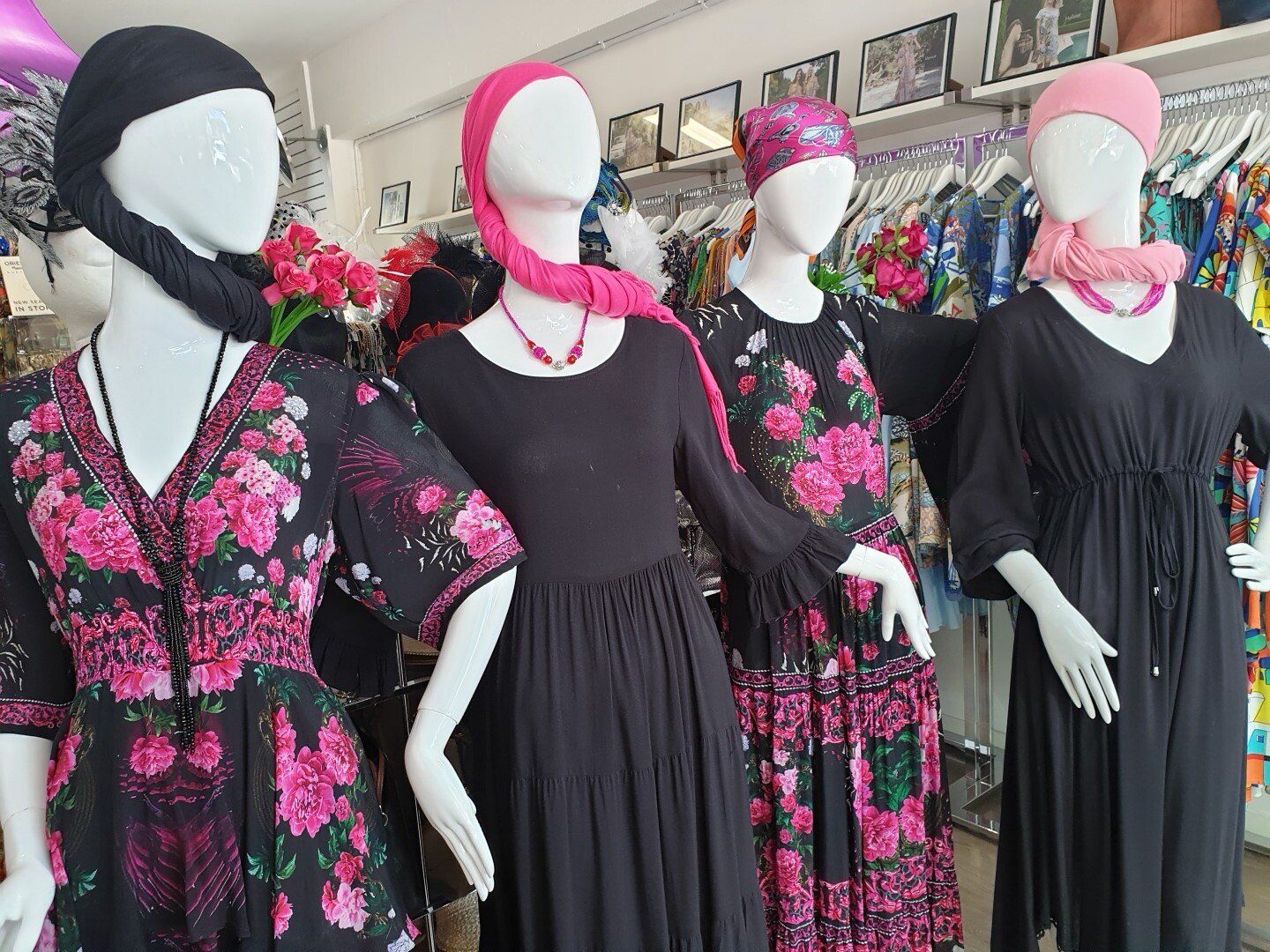 Four mannequins in a clothing store, wearing black dresses with pink floral patterns and scarves.