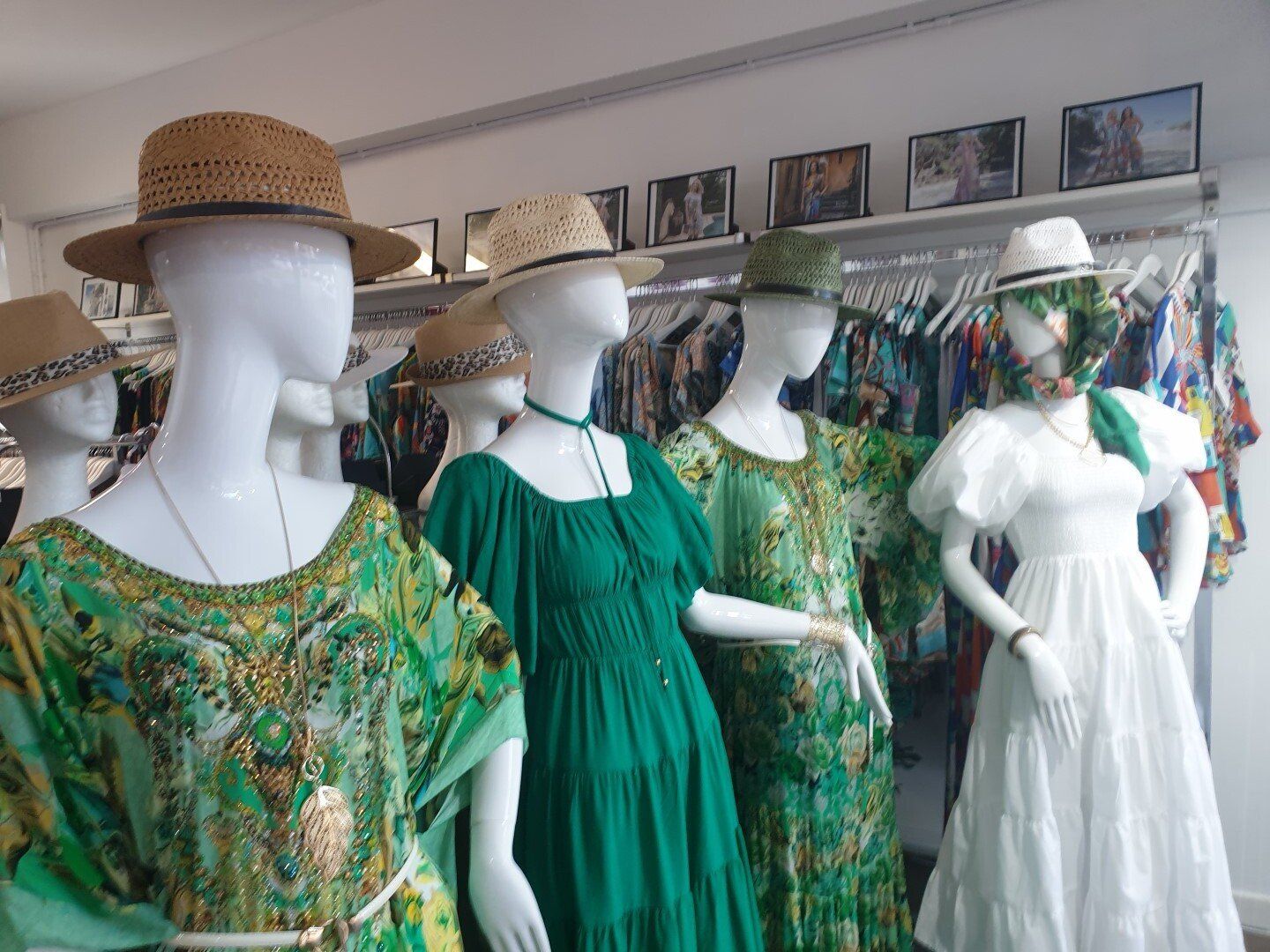 Mannequins in a store display dresses and hats; green and white colors are prominent.
