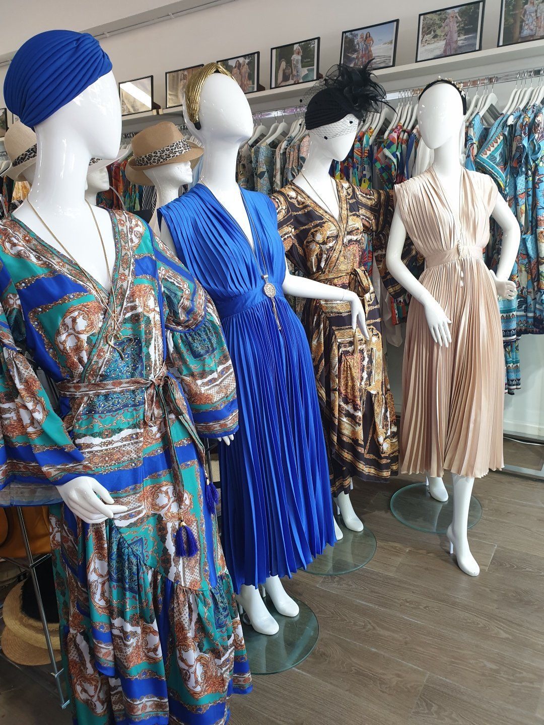 Mannequins in a clothing store, showcasing dresses: blue, brown, and tan. Hats and jewelry on display.