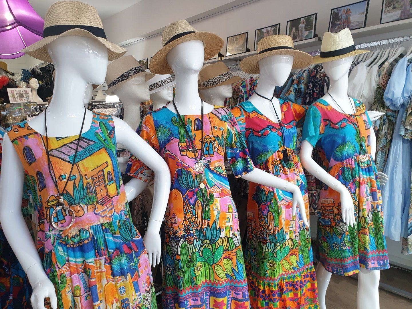 Mannequins in colorful patterned dresses and straw hats, inside a shop.