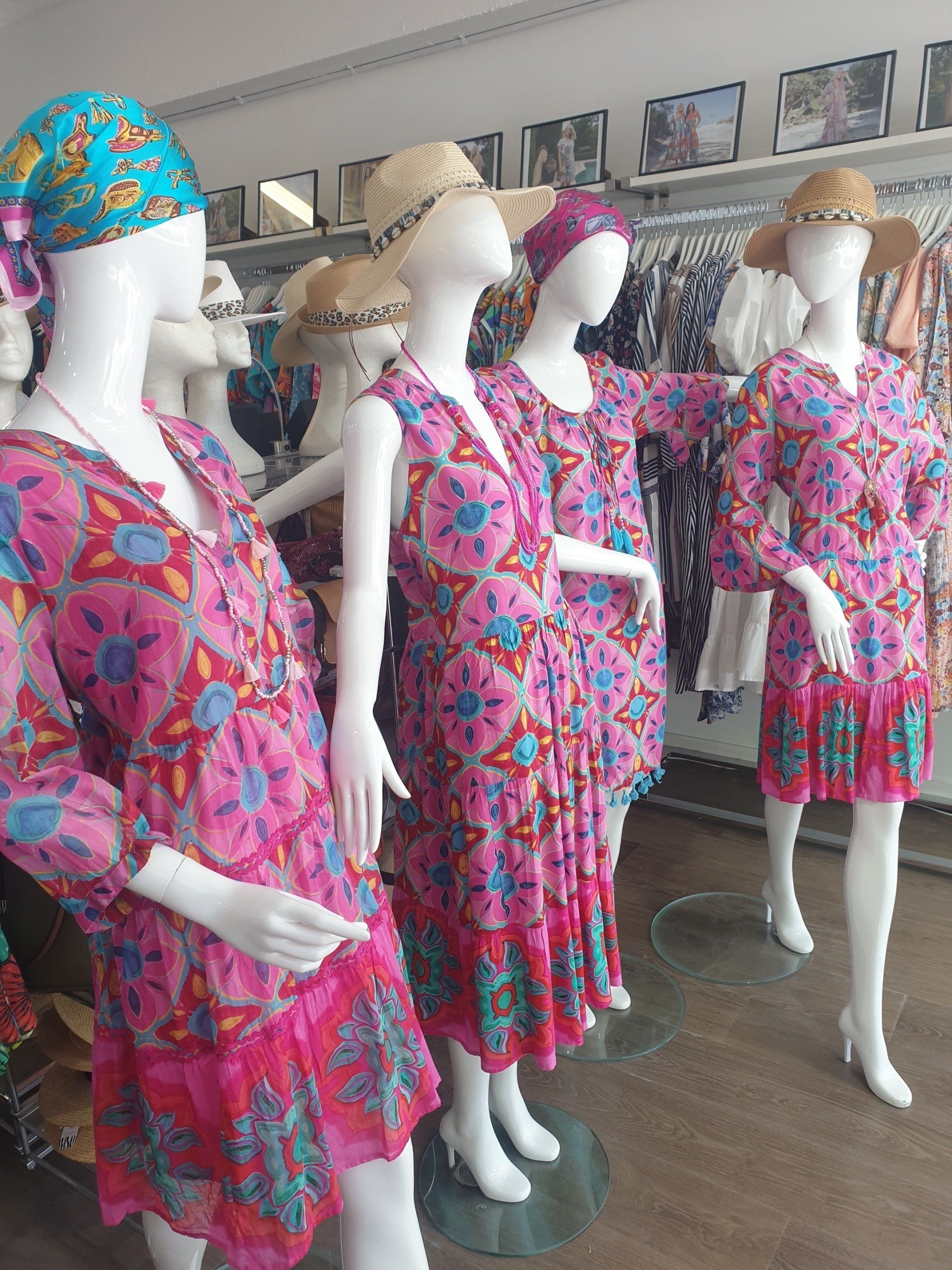 Mannequins in a boutique wearing pink floral dresses and hats; a retail setting.