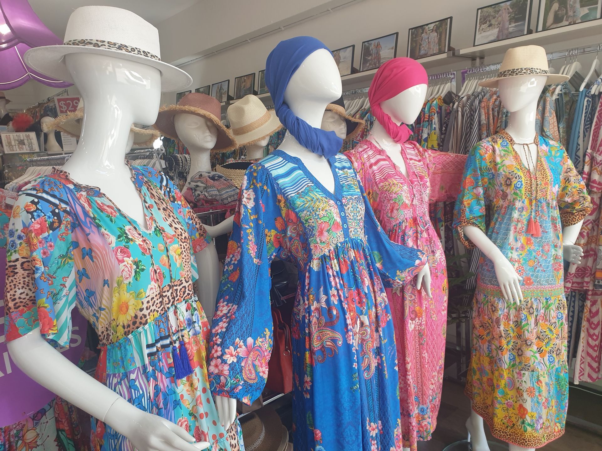 Mannequins in a clothing store wearing colorful floral dresses and hats.